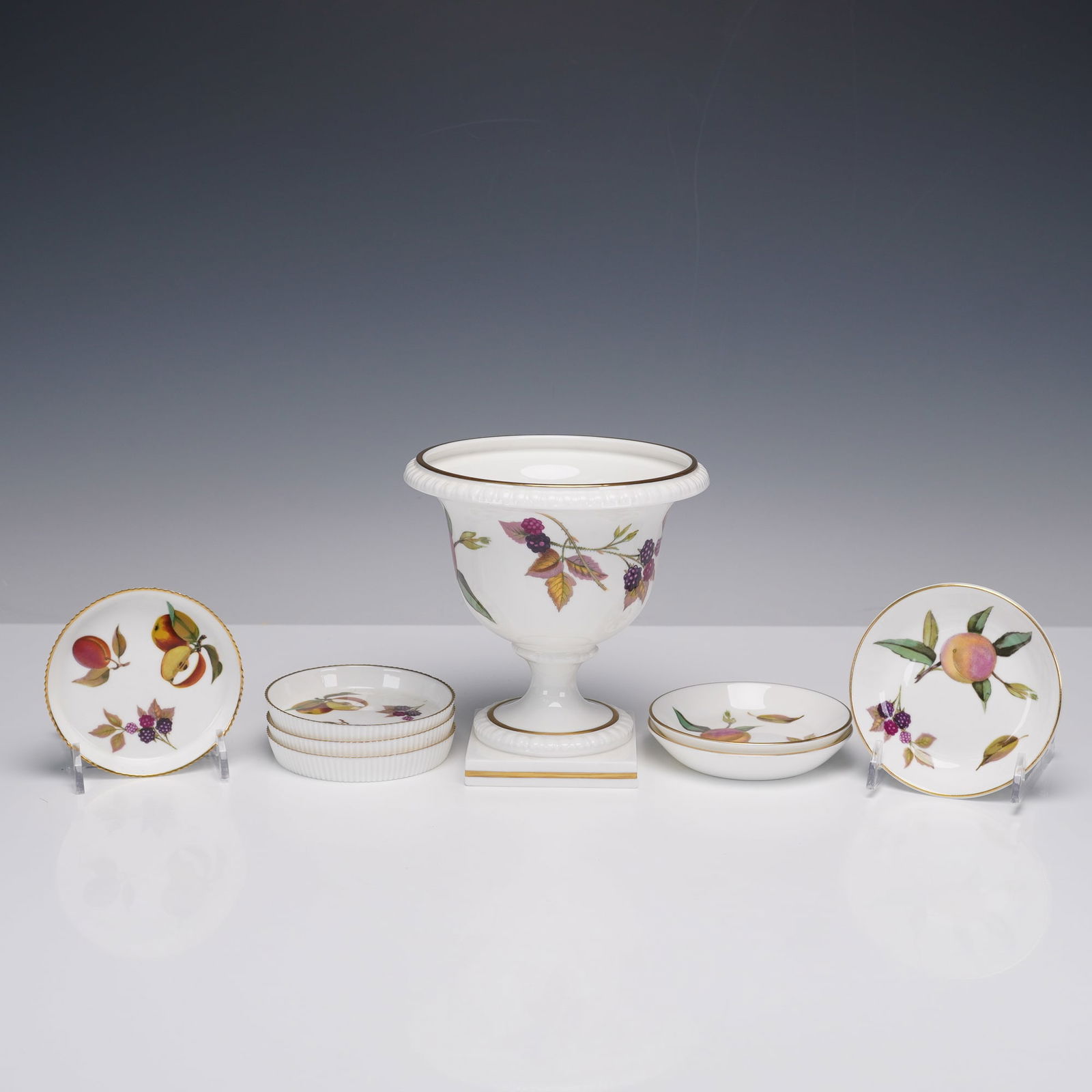 8pc Royal Worcester Bone China Vase, Ash Trays, and Coasters, Arden: The collection is crafted from white bone china and features detailed fruit motifs, each piece finished with gilt trim. Included are a footed urn vase with a square base, three small round ash trays w