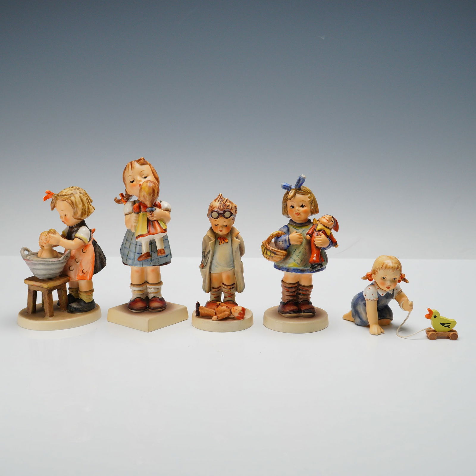 5pc Goebel Hummel Figurines, Play Day: Charming set of five Goebel Hummel figurines celebrating childhood play and imagination. Includes Doctor 127, depicting a boy in spectacles examining a doll patient; Just Lucky 2278, with a girl proud