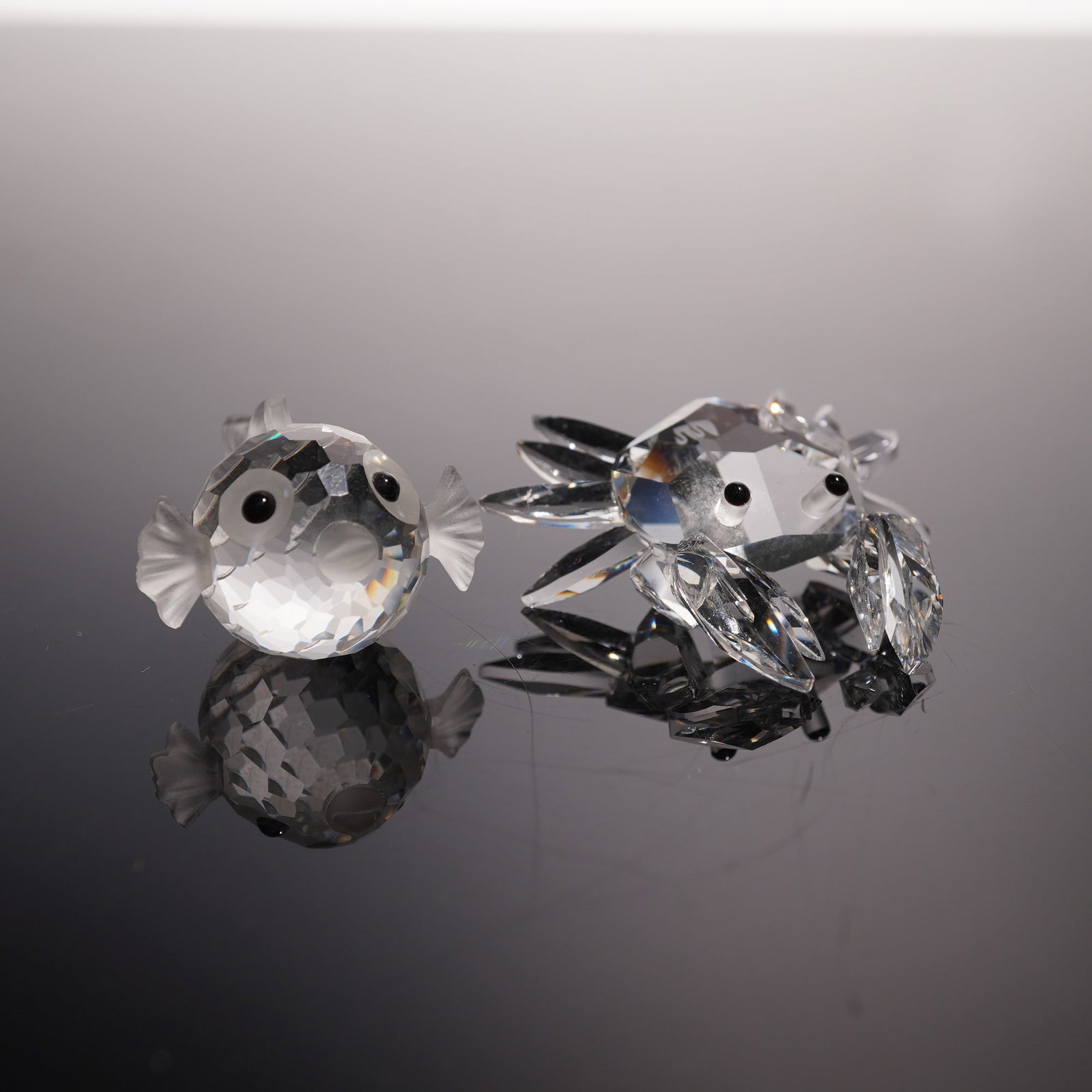 2pc Swarovski Silver Crystal Figurines, Mini Blowfish and Mini Crab: Set of two silver crystal figurines comprising a round bodied blowfish and a detailed crab, each executed in precisely faceted crystal. The fish displays a spherical form with textured fins and tail r