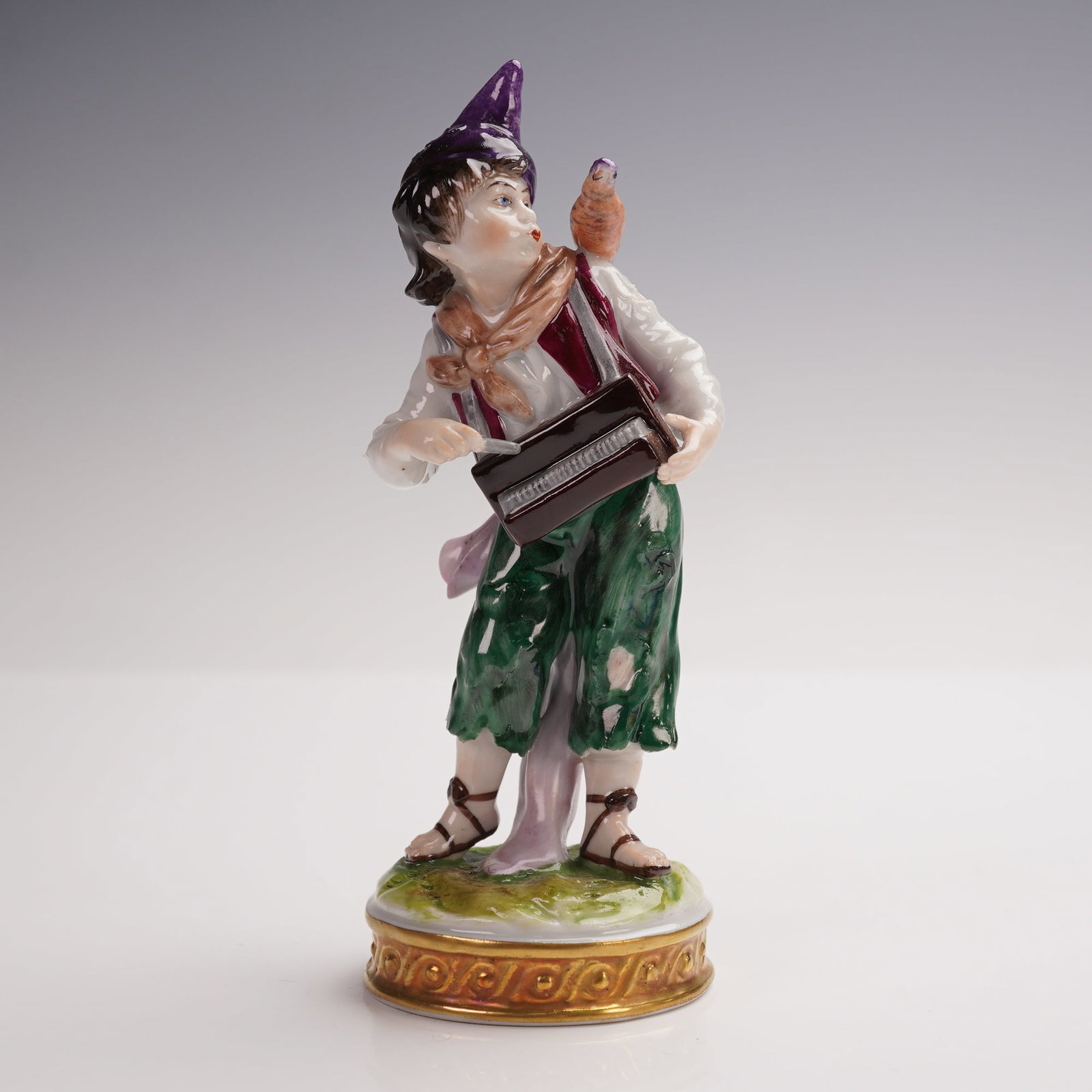 Capodimonte Accordion Player Figurine: Porcelain figurine depicting an accordion player with a bird perched on his shoulder. The figure is dressed in a pointed purple hat, green trousers, white shirt, and burgundy vest, accented with a sca