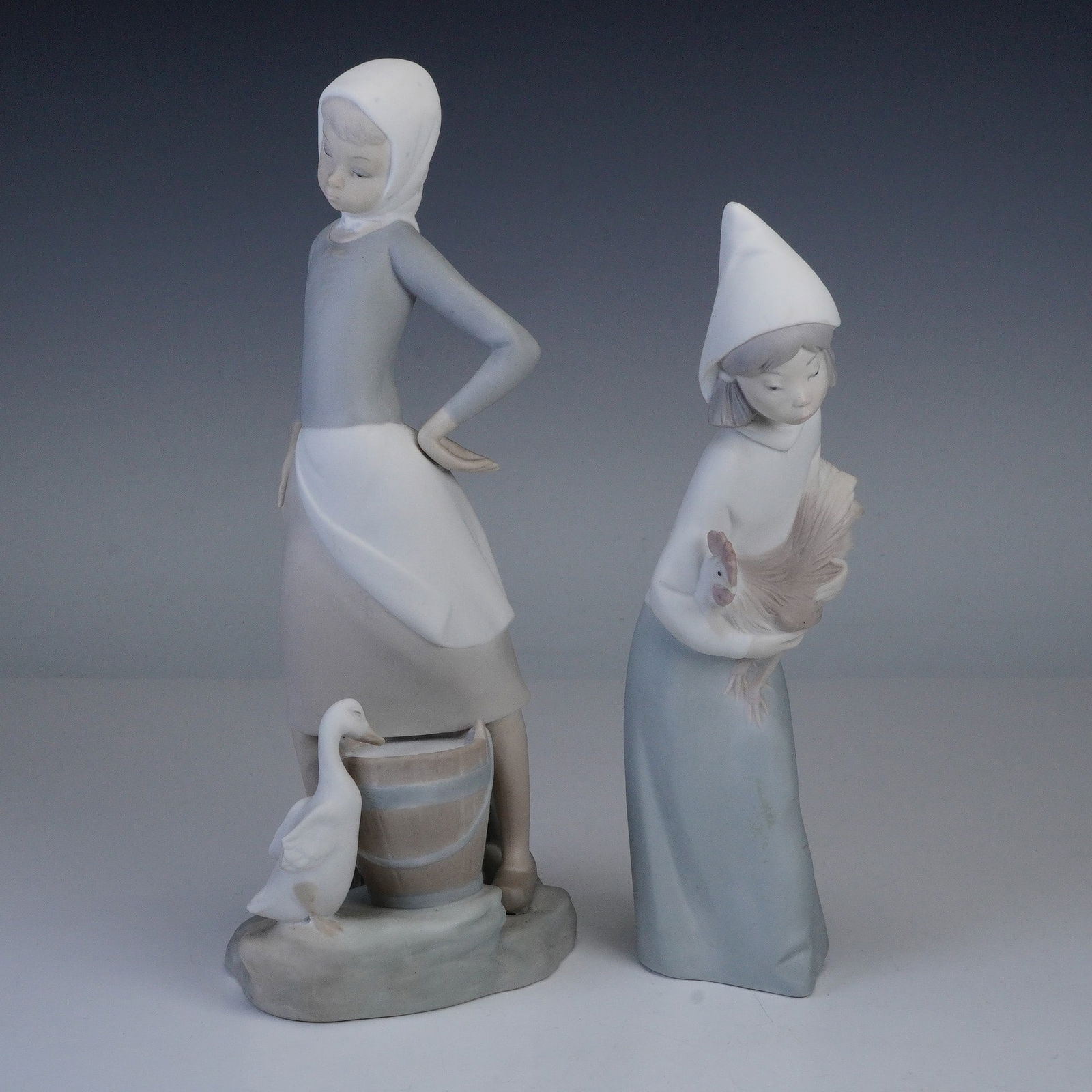 Lladro Porcelain Figurines, Girl w/ Milk Pail & Girl w/ Rooster: Lladro porcelain figurines, two pieces, titled Girl with Milk Pail 1014682 and Girl with Rooster 1014677, both presenting a matte finish. Girl with Milk Pail depicts a young girl in a headscarf and ap