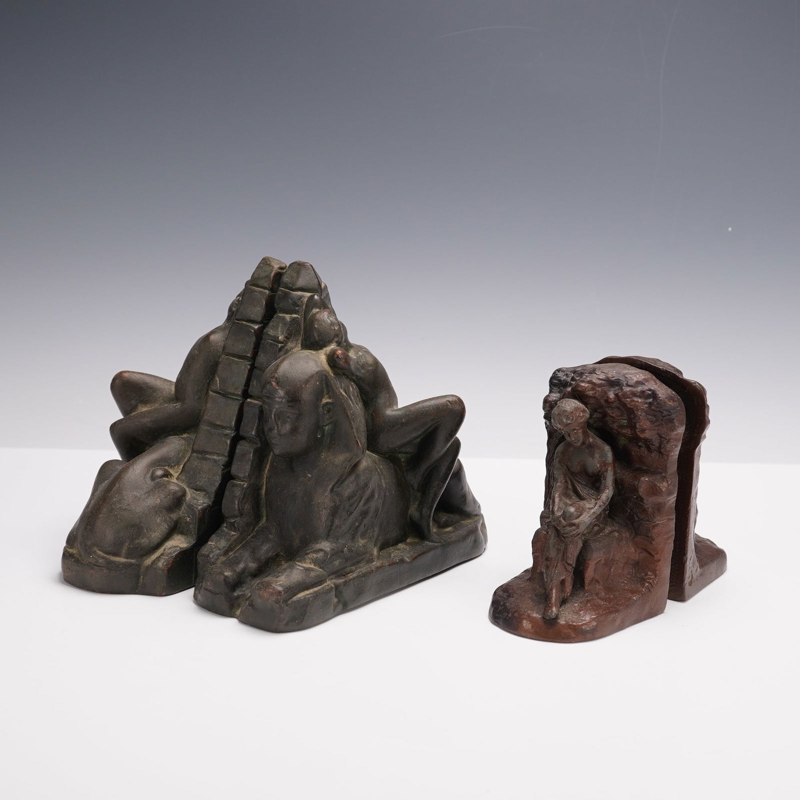 4pc Egyptian Revival and Classical Cast Metal Figural Bookends: A group of two pairs of cast metal figural bookends, four pieces total. One pair in the Egyptian Revival style depicts a reclining nude figure draped across the back of a sphinx with a pyramid rising