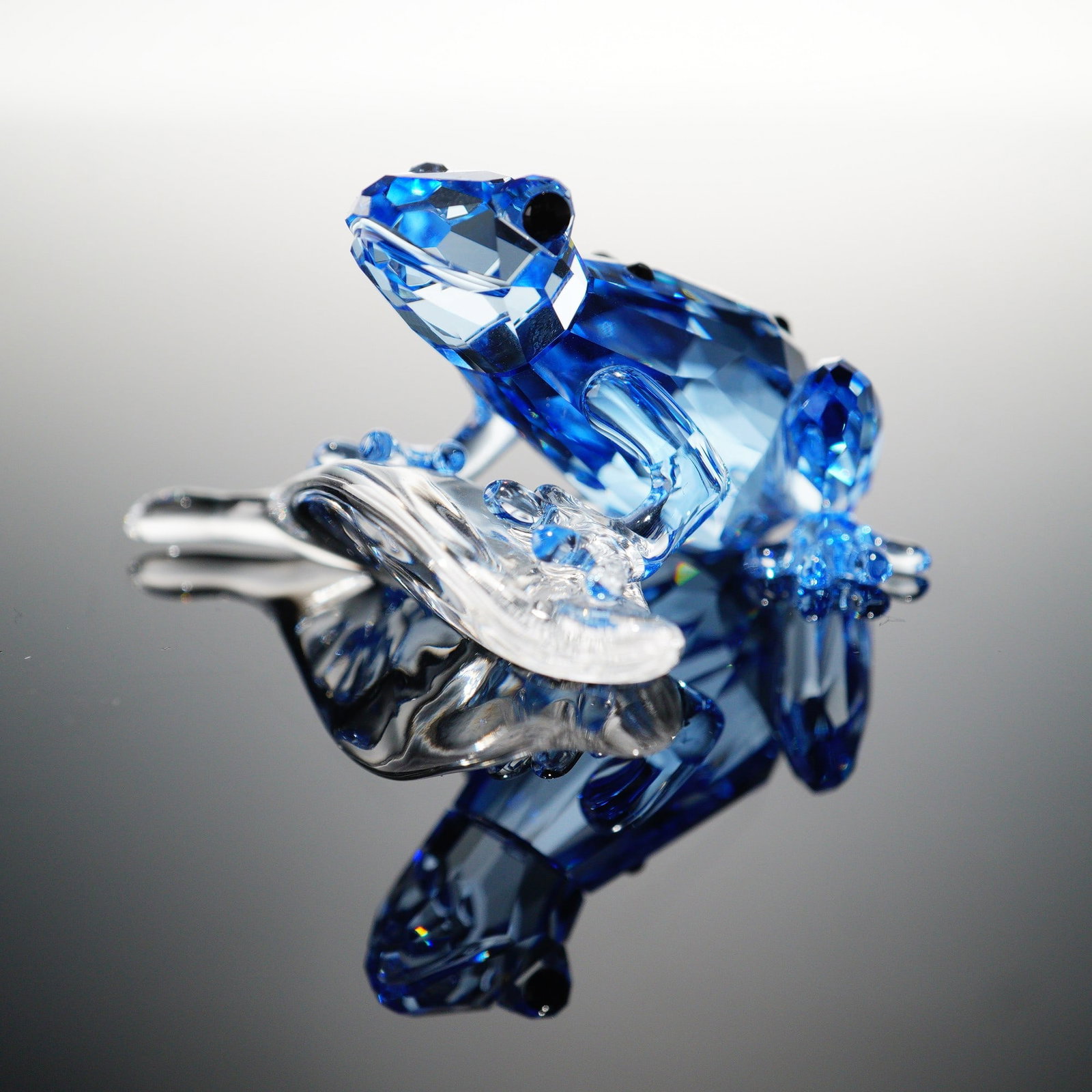 Swarovski Crystal Figurine, Dart Frog: A Swarovski Crystal figurine of a dart frog, crafted in light blue faceted crystal with black crystal accents. Designed as the 2009 Swarovski Event Piece, this collectible is mounted on a clear crysta