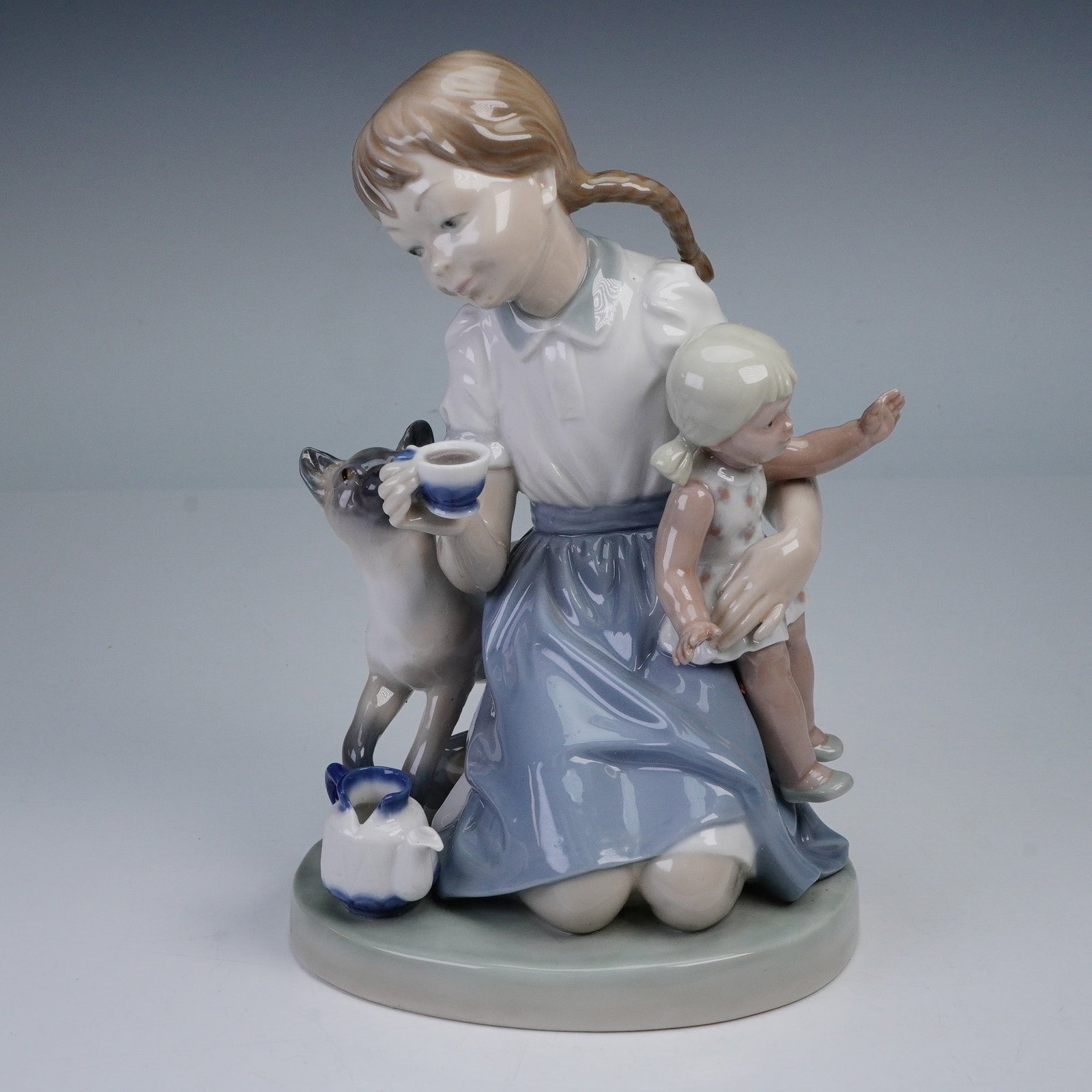 Lladro Porcelain Figurine, Child's Play 01001280: This delightful Lladro figurine, Child's Play, beautifully captures the innocence of childhood. Sculpted by Salvador Furio, the piece features a young girl playing with a child and a cat, all in a ser