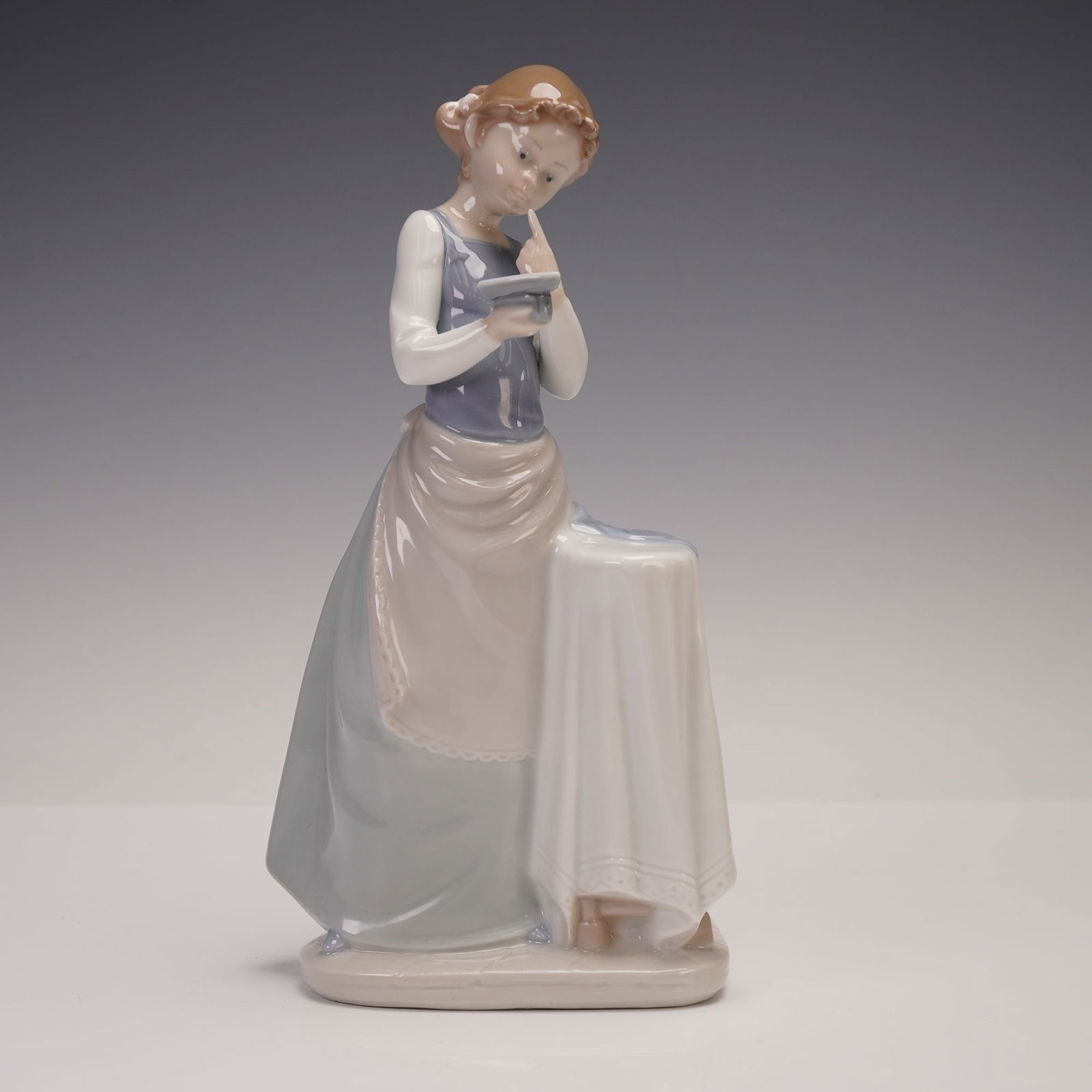 Lladro Vintage Figurine, Girl Ironing 1004981: This charming porcelain piece depicts a young girl thoughtfully engaged in ironing, standing beside a covered table with an iron in her hand. She is dressed in a long flowing skirt with apron and blou