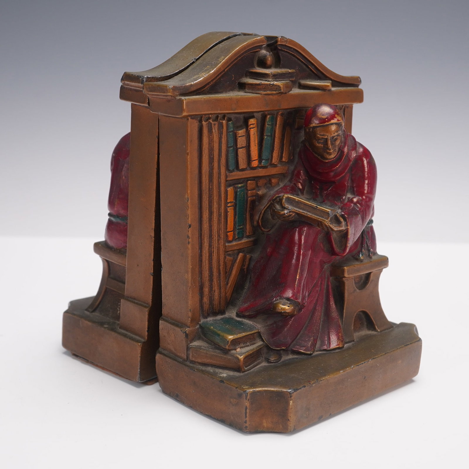Pair of Ronson Metal Bookends, Bronze-clad Monk Reading: Each piece shows the robed figure in deep concentration, holding an open book with additional books at his feet, the scene framed by an arched library backdrop. Richly detailed with polychrome accents
