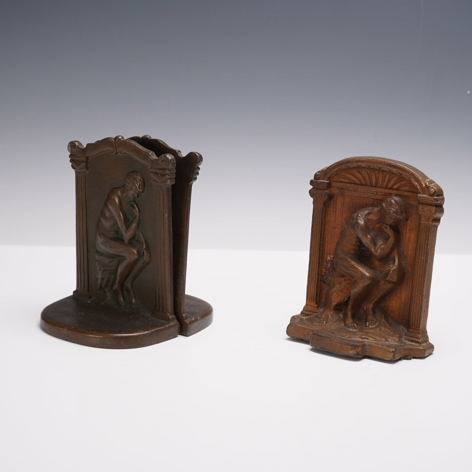 3pc Cast Metal Figural Bookends, The Thinker: A group of three cast metal figural bookends depicting Auguste Rodin's The Thinker. Includes a matched pair featuring the seated male figure in deep contemplation within an architectural frame, togeth