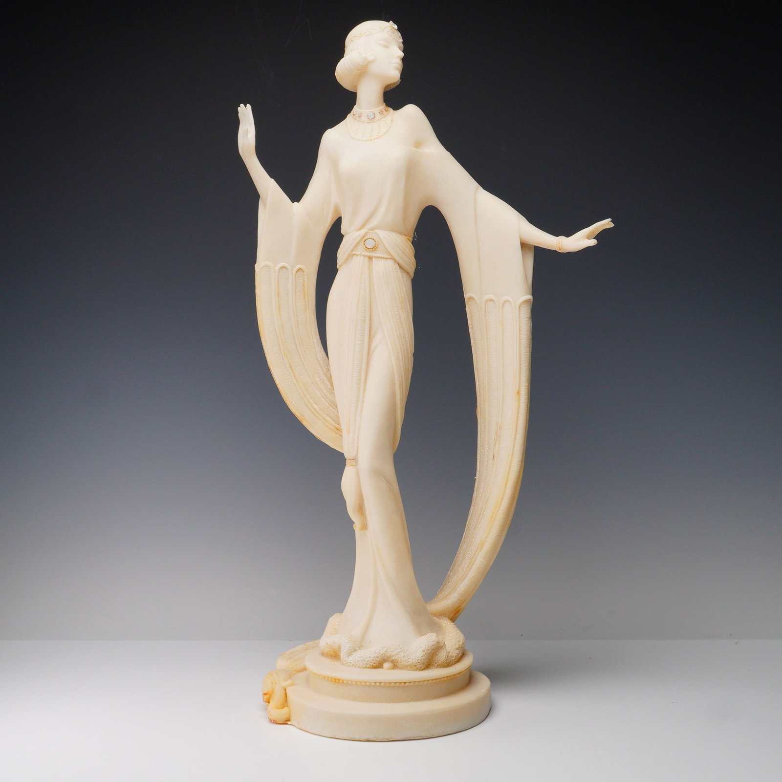 Art Deco Style Lady Sculpture: A tall decorative sculpture in the Art Deco style, portraying an elegant woman in a long gown with stylized sleeves and detailed jewelry. The piece is modeled with refined features and flowing lines, 