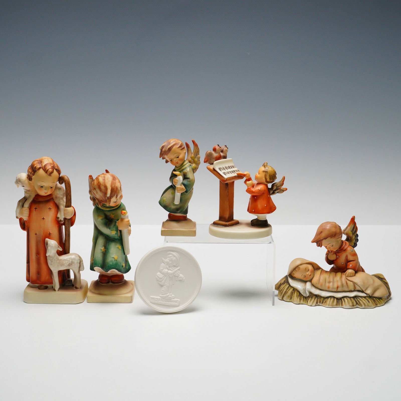 6pc Goebel Hummel Figurines and Plaque: The collection includes five figures: "Good Shepherd" (HUM42/0) depicting a young shepherd with lamb, "Bird Duet" (HUM169) featuring angels with birds and music stand, "Angelic Sleep"(HUM25) showing a