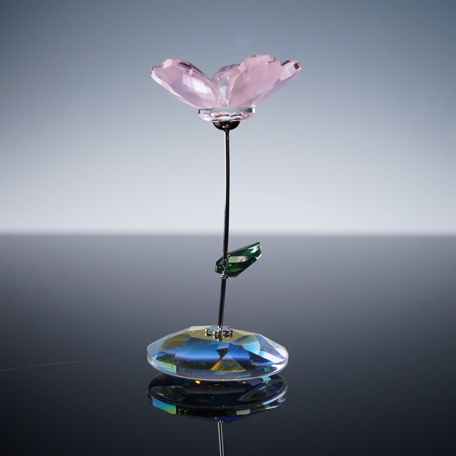 Swarovski Crystal Rocking Flower Figurine, Kay Rose: Featuring a wild rose with faceted petals crafted from rosaline moonlight crystal and a white opal crystal bead at the center. The flower is accented with a faceted erinite crystal leaf attached to a 