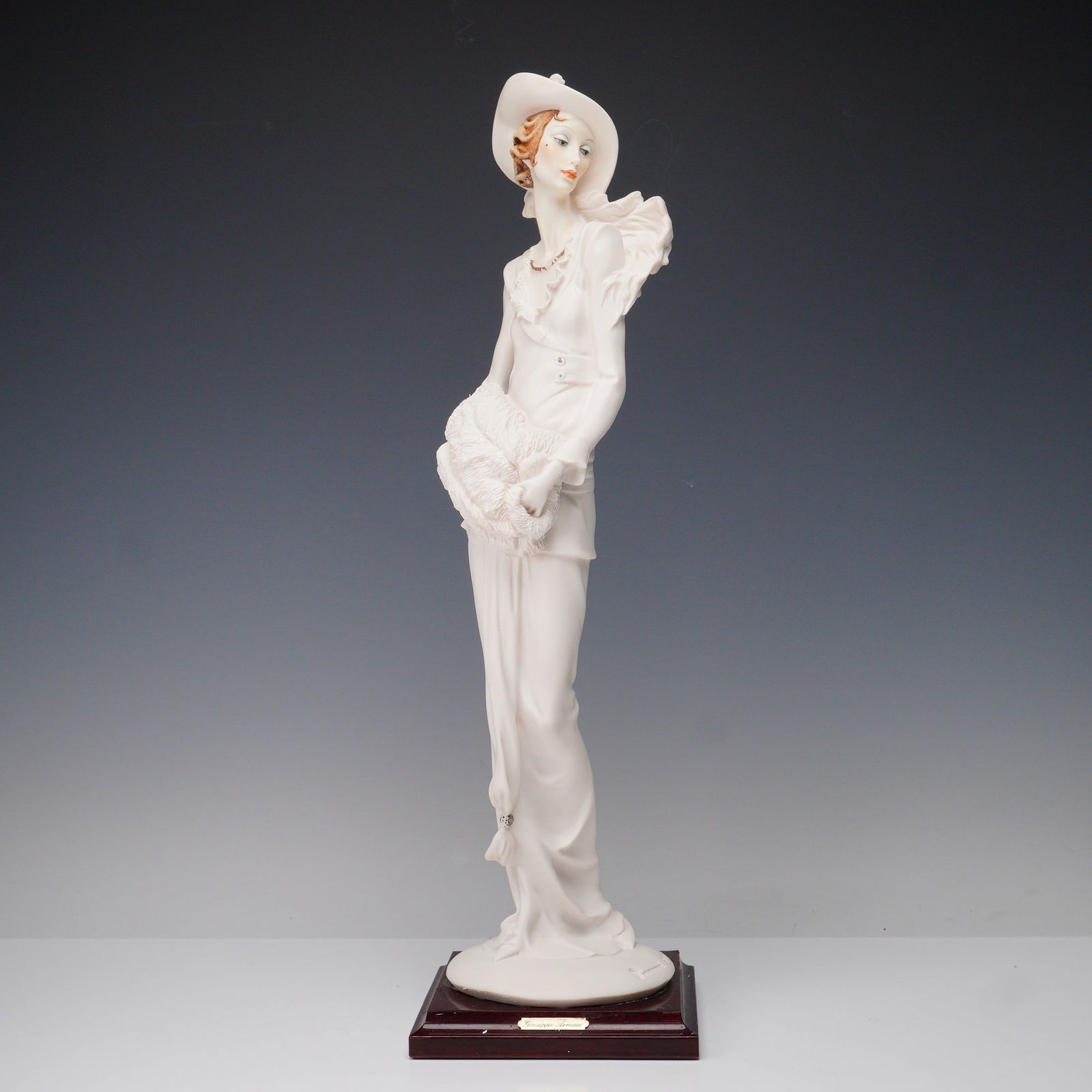 Giuseppe Armani Florence Capodimonte Lady with Hat and Muff Figurine: This finely crafted figurine by Giuseppe Armani for the Florence studio depicts a stylish lady in a wide brimmed hat holding a fur muff. The piece shows Armani's trademark attention to detail, from th