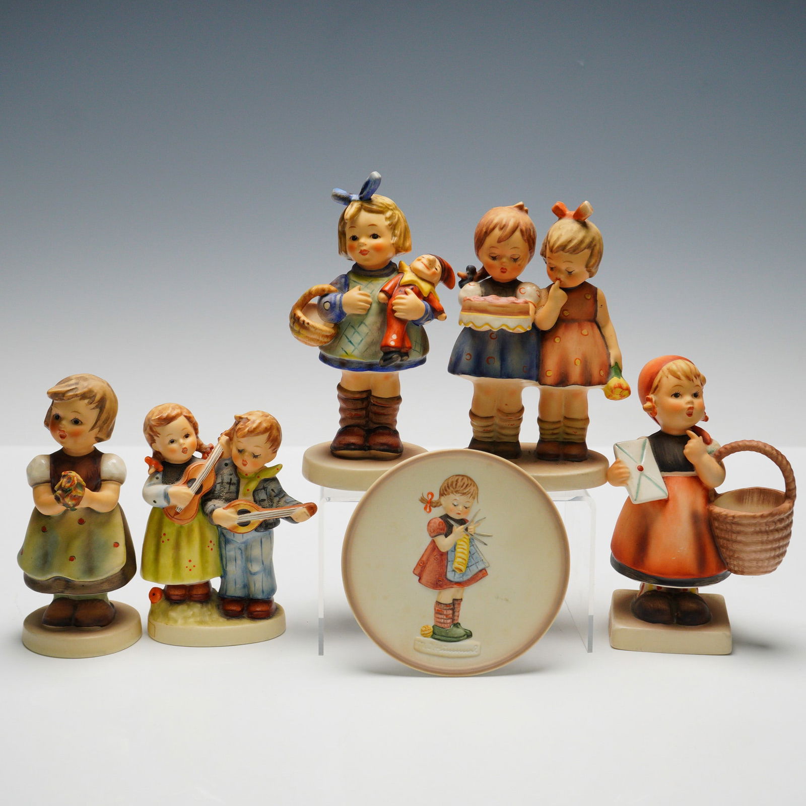 6pc Goebel Hummel Figurines and Plaque: Collection includes five figurines and one round plaque. Figurines consist of "Happy Days" (HUM150 2/0) depicting a boy and girl with string instruments, "Happy Birthday" (HUM176/0) with two girls hol