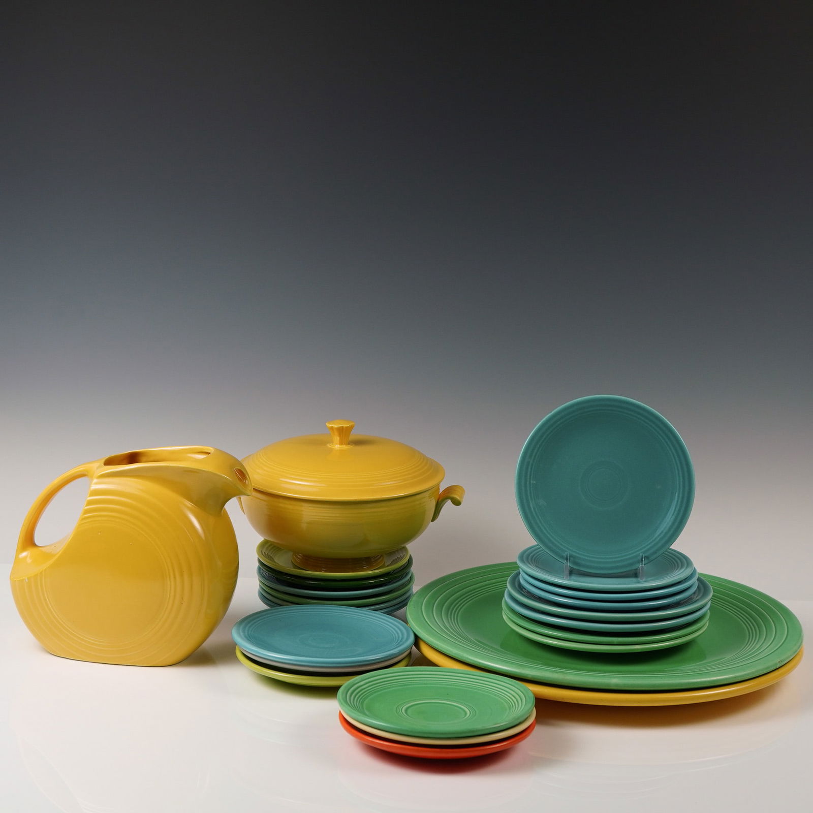 Fiesta Ware Lot with Marigold Pitcher and Covered Casserole: A vibrant 24-piece collection of vintage Fiesta dinnerware, including two hard-to-find charger plates, one iconic marigold disk water pitcher, and one matching marigold covered casserole dish with scr