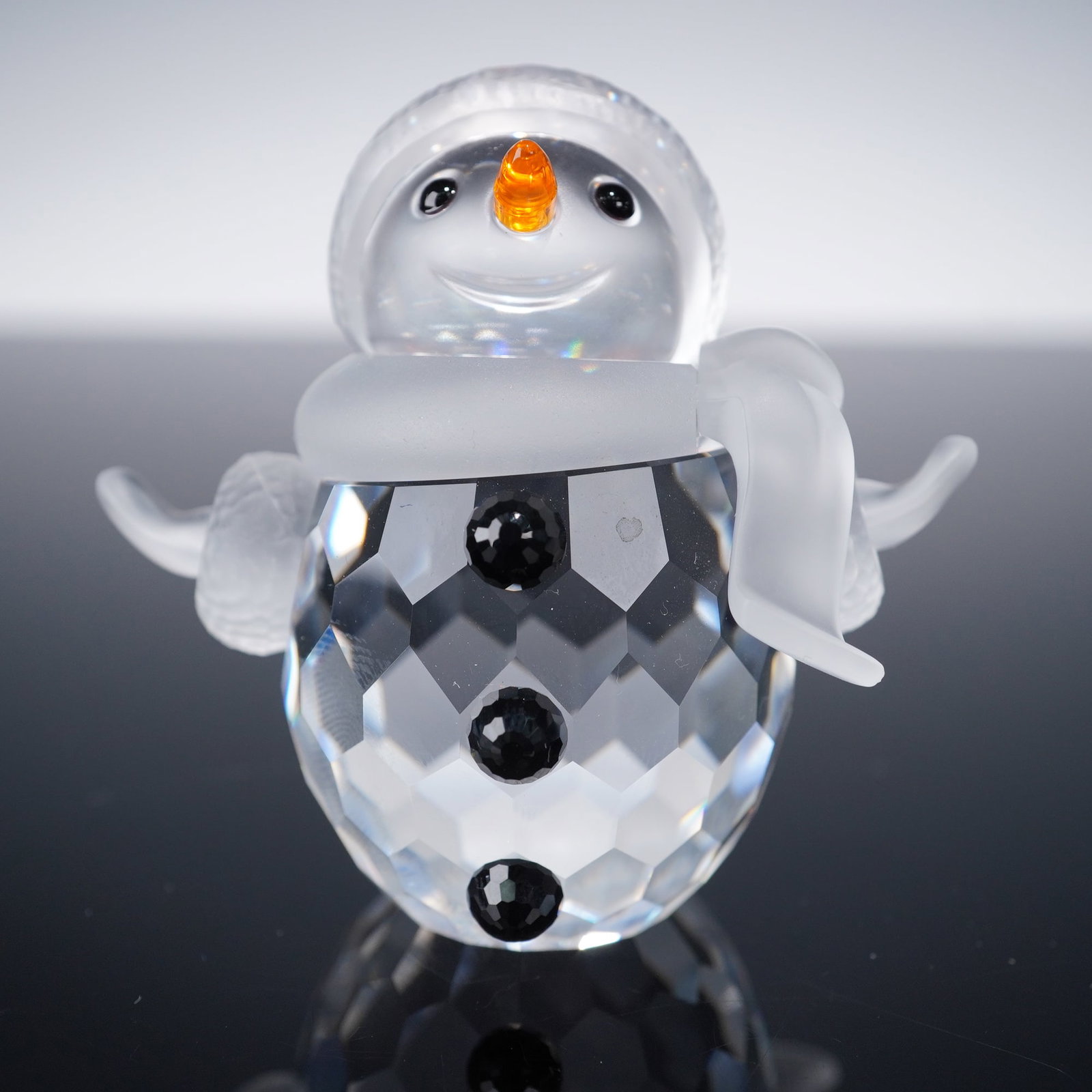 Swarovski Cheerful Times Crystal Figurine, Snowman: A charming crystal snowman from the Cheerful times collection, featuring a brilliantly faceted clear crystal body accented with three jet-black crystal buttons. The snowman wears a frosted crystal hat