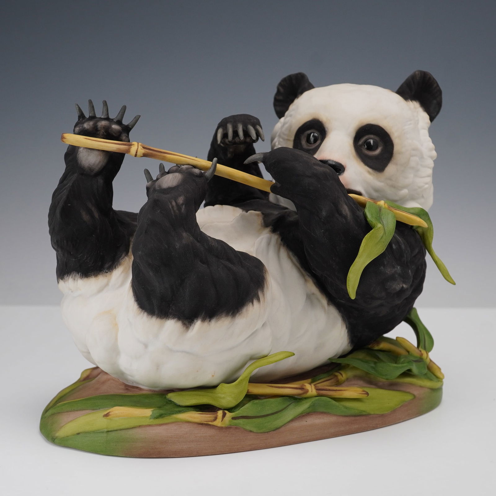 Boehm Porcelain Figurine, Giant Panda Cub: A playful young panda lying on its back while clutching a bamboo stalk with lively expression and finely detailed features. Handcrafted in the United States by the Edward Marshall Boehm studios, the p