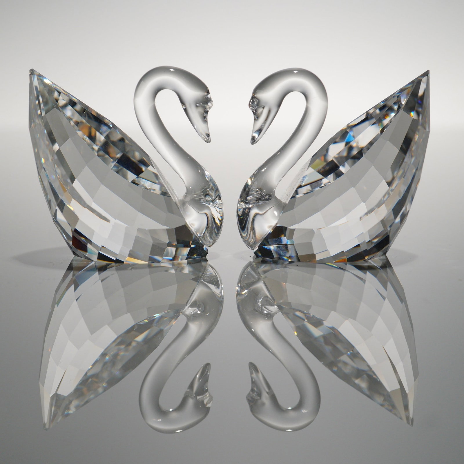 2pc Swarovski Crystal Swan Figurines: Two faceted Swarovski crystal swans with frosted detailing to the neck and head. Both pieces are marked with the Swarovski swan logo. One figurine is accompanied by its original box, while the other i