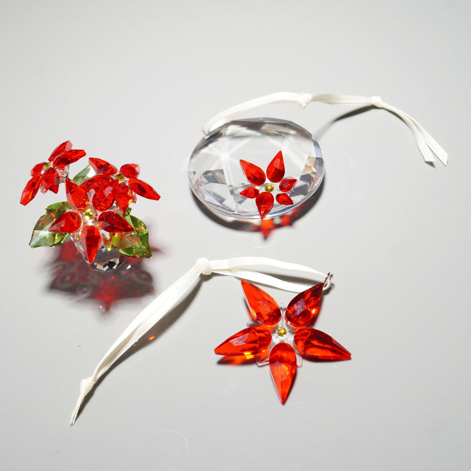 3pc Swarovski Crystal Poinsettia Ornaments and Figurine: Festive Swarovski Crystal lot including two poinsettia Christmas ornaments and one poinsettia figurine. Each piece is crafted with vibrant red crystal petals accented with a golden center. Both orname
