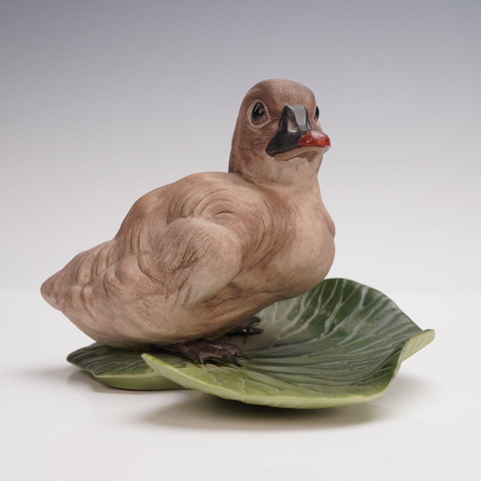 Boehm Porcelain Figurine, Cygnet: A fine and detailed porcelain sculpture by Boehm, titled Cygnet and numbered 400-46. This charming figurine depicts a young swan resting upon a green lily pad base, rendered with remarkable naturalist