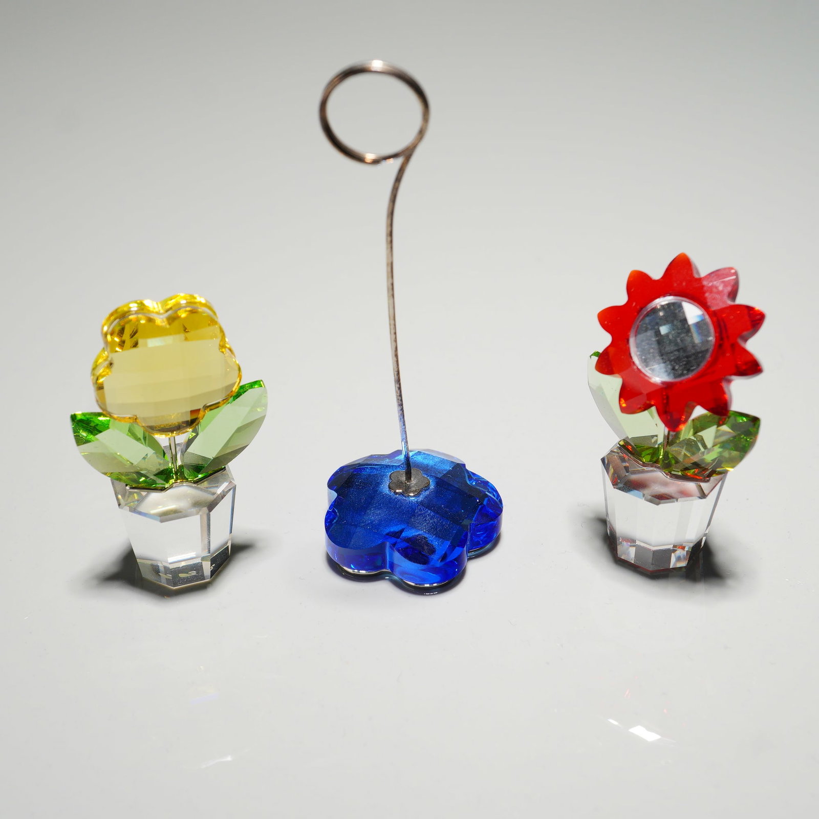 3pc Swarovski Crystal Flower Figurines and Note Holder: A colorful group of Swarovski crystal creations including an Aster figurine with red petals, a Yellow Flower figurine with green leaves, and a sapphire-blue Flower note holder with silvertone stem. Ea