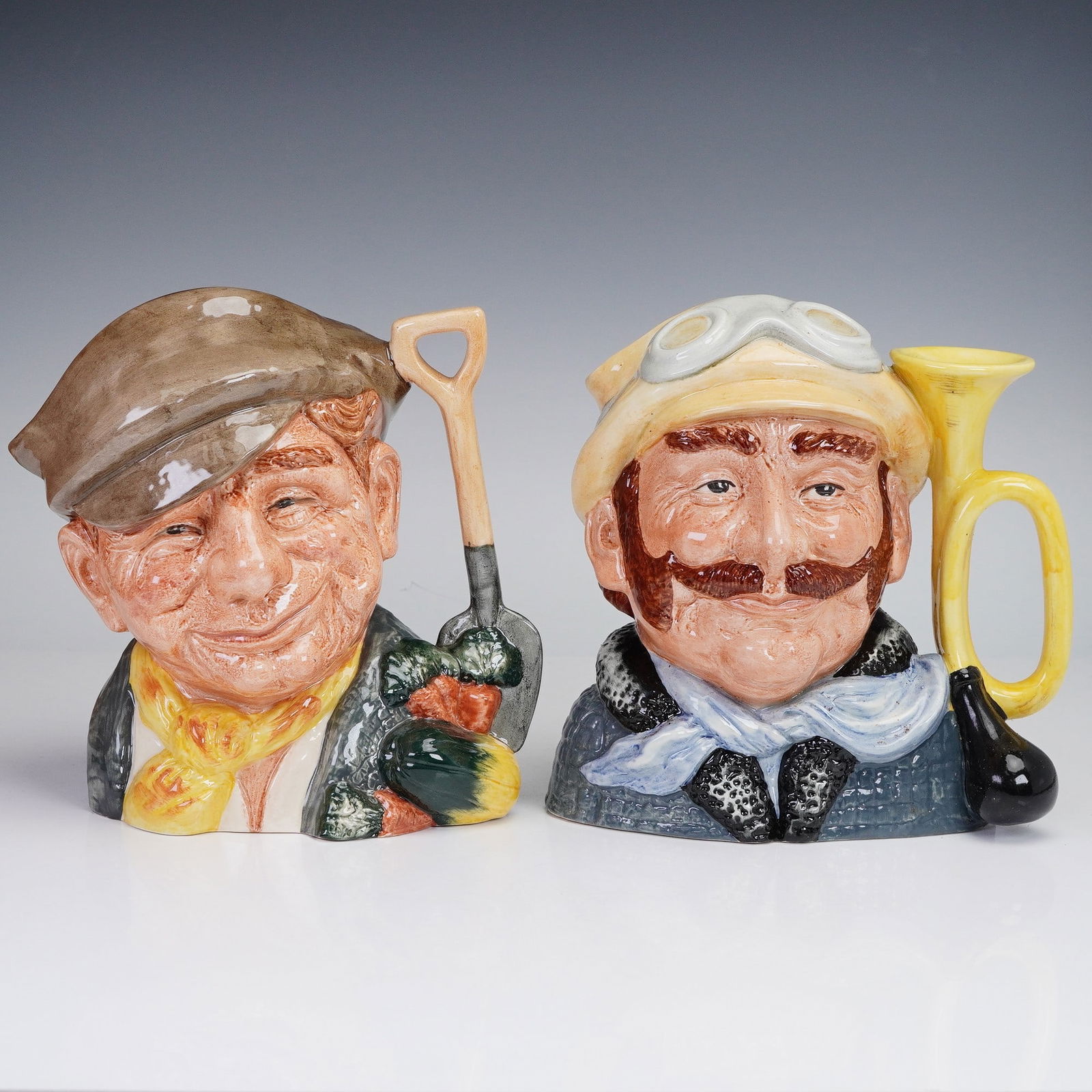 2pc Royal Doulton Character Jug Set Gardener Old D6630 and Veteran Motorist: This set includes two large Royal Doulton character jugs designed by David B. Biggs. The Gardener jug, issued from 1973 to 1981, features a yellow scarf, white shirt, and light brown hat. The Veteran