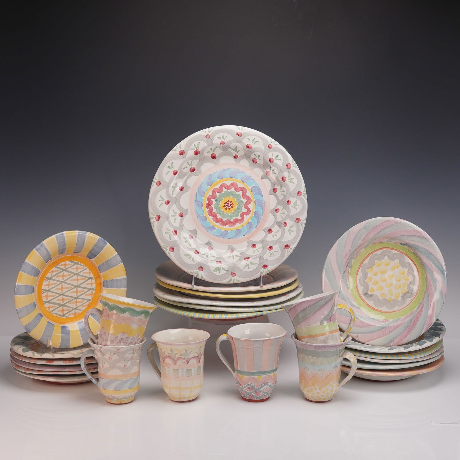 24pc Victoria and Richard MacKenzie-Childs Plates and Teacups: A vibrant hand painted pottery service by Victoria and Richard Mackenzie Childs including six mugs, six salad plates, six dinner plates, and six bowls. Each piece is richly decorated in the makers sig