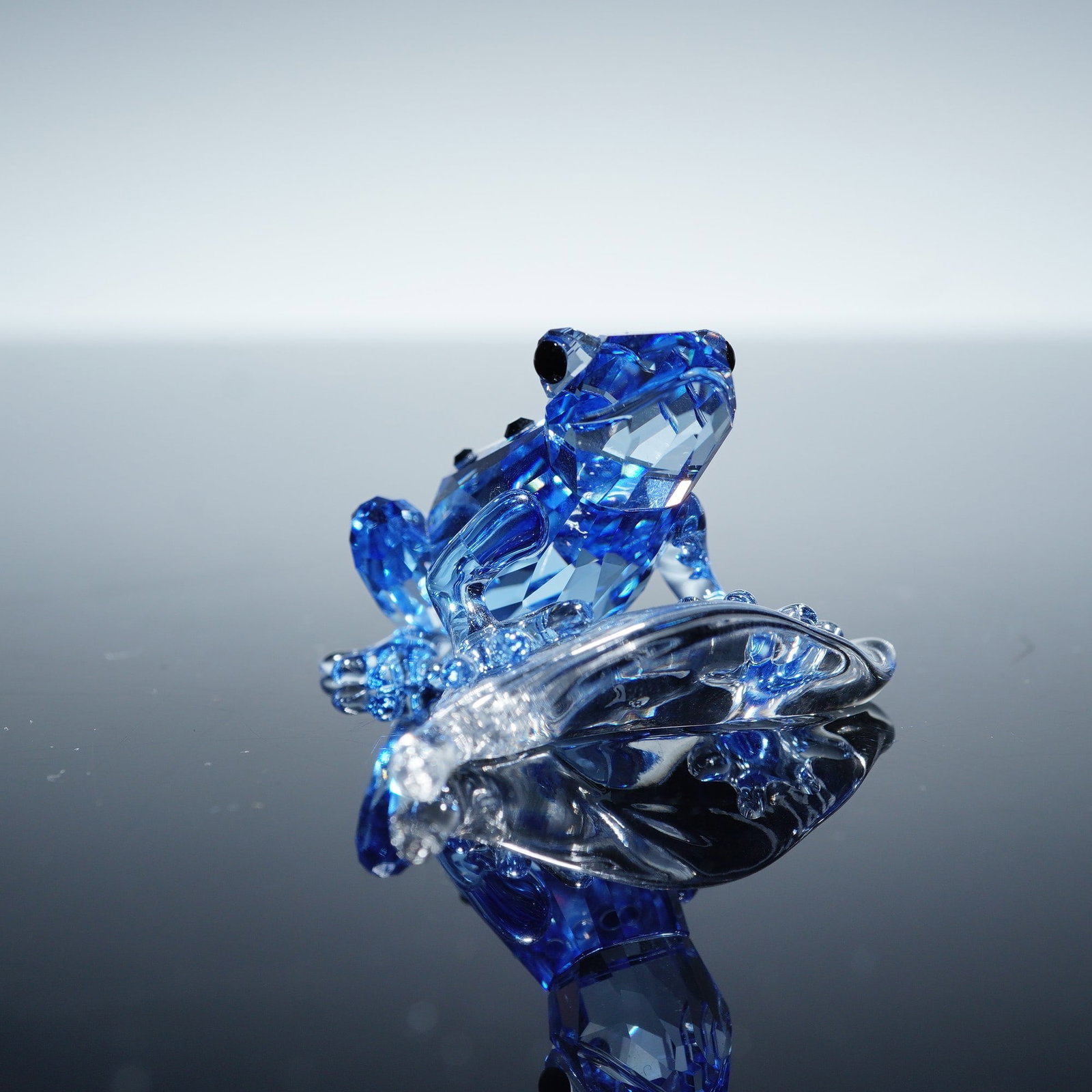 Swarovski Crystal Figurine, Dart Frog: A Swarovski Crystal figurine of a dart frog, crafted in light blue faceted crystal with black crystal accents. Designed as the 2009 Swarovski Event Piece, this collectible is mounted on a clear crysta