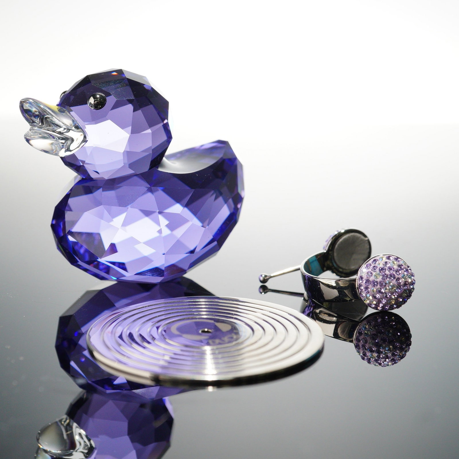 Swarovski Crystal Figurine, Happy Duck J: A vibrant Swarovski Happy Ducks creation featuring Duck J, crafted in blue violet crystal with a Moonlight crystal beak. This playful duck is accessorized with sparkling purple crystal headphones and 