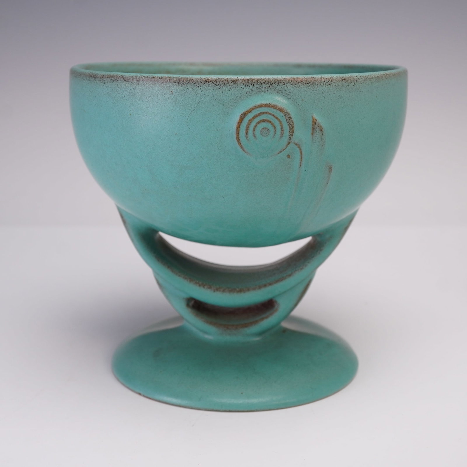 Roseville Pottery Blue Footed Bowl, Moderne: Art Deco footed bowl in turquoise-blue glaze, featuring a stylized geometric cut-out pedestal base and a circular swirl motif on the bowl's exterior. The matte glaze shows subtle variations in tone wi