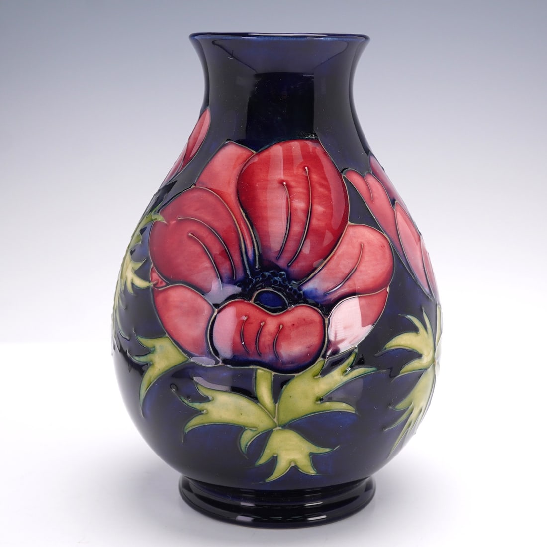 Moorcroft Pottery Vase, Anemone: Featuring a cobalt-blue ground with tube-lined decoration of anemone flowers in shades of red, purple, and green. The underside bears the impressed Moorcroft stamp, along with the WM monogram. The bas