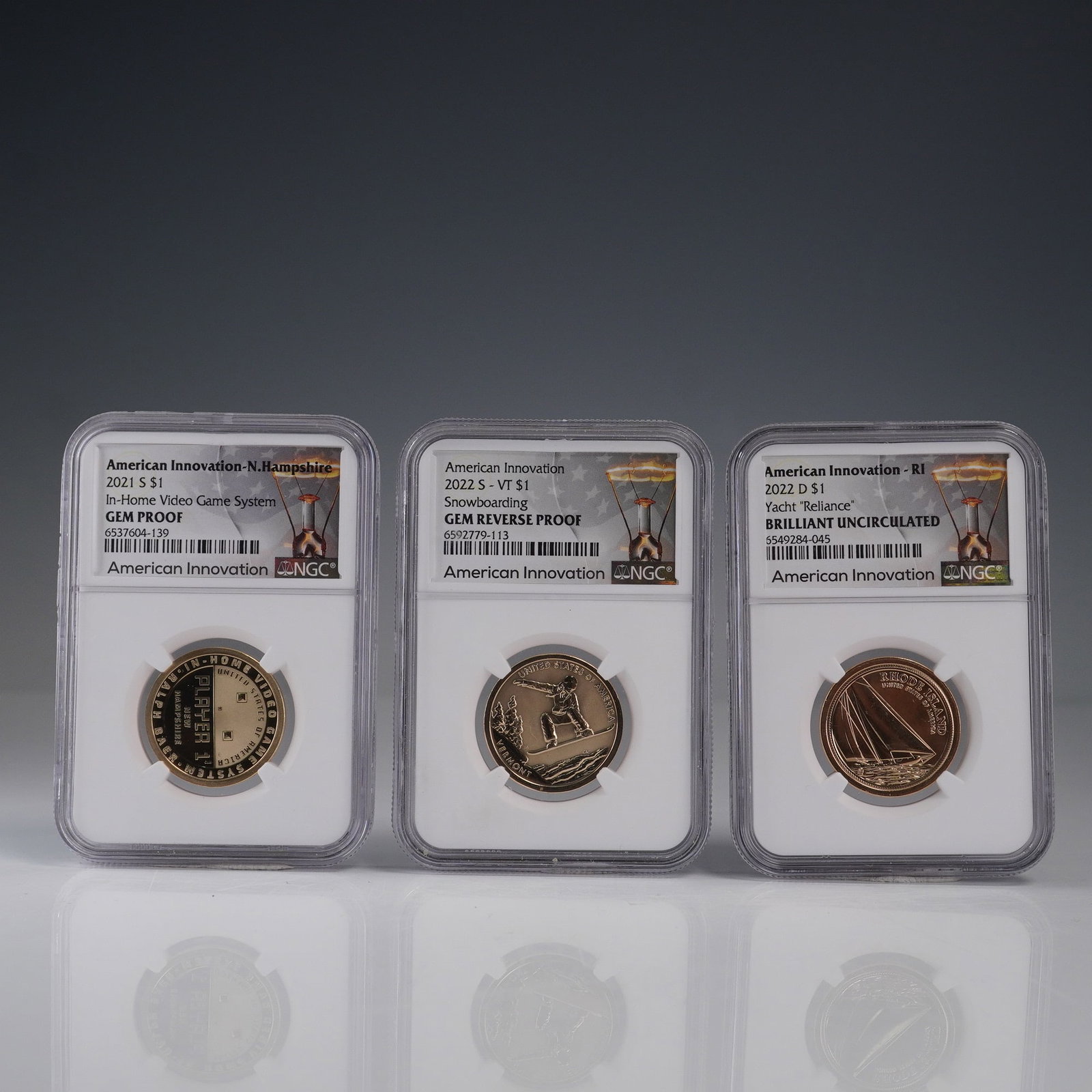 3pc American Innovation Dollar Coins, New Hampshire, Vermont & Rhode Island: A group of three American Innovation series dollar coins, each certified by NGC. Includes a 2021 S New Hampshire coin featuring the In-Home Video Game System in GEM PROOF, a 2022 S Vermont coin depict