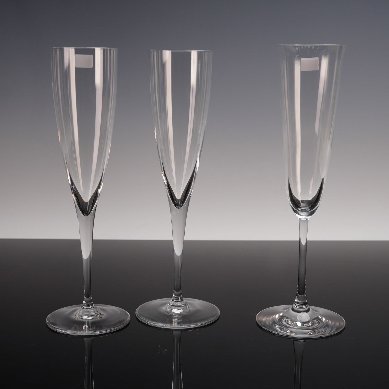 3pc Baccarat Crystal Champagne Glasses: A refined collection of three crystal champagne flutes. Each flute features a tall and slender profile with elongated bowls tapering gracefully into faceted stems and broad circular bases. Baccarat st