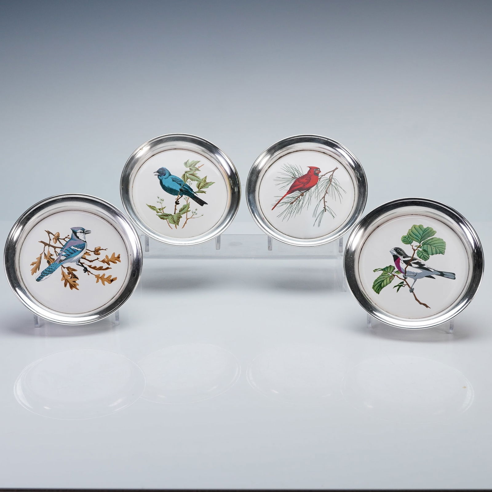 4pc Sheridan Silver Co. Silverplate Coasters: Four pleasant coasters, each inset with a decorative ceramic tile depicting a different bird species rendered in vivid coloration. Includes a cardinal, blue jay, indigo bunting, and rose-breasted gros