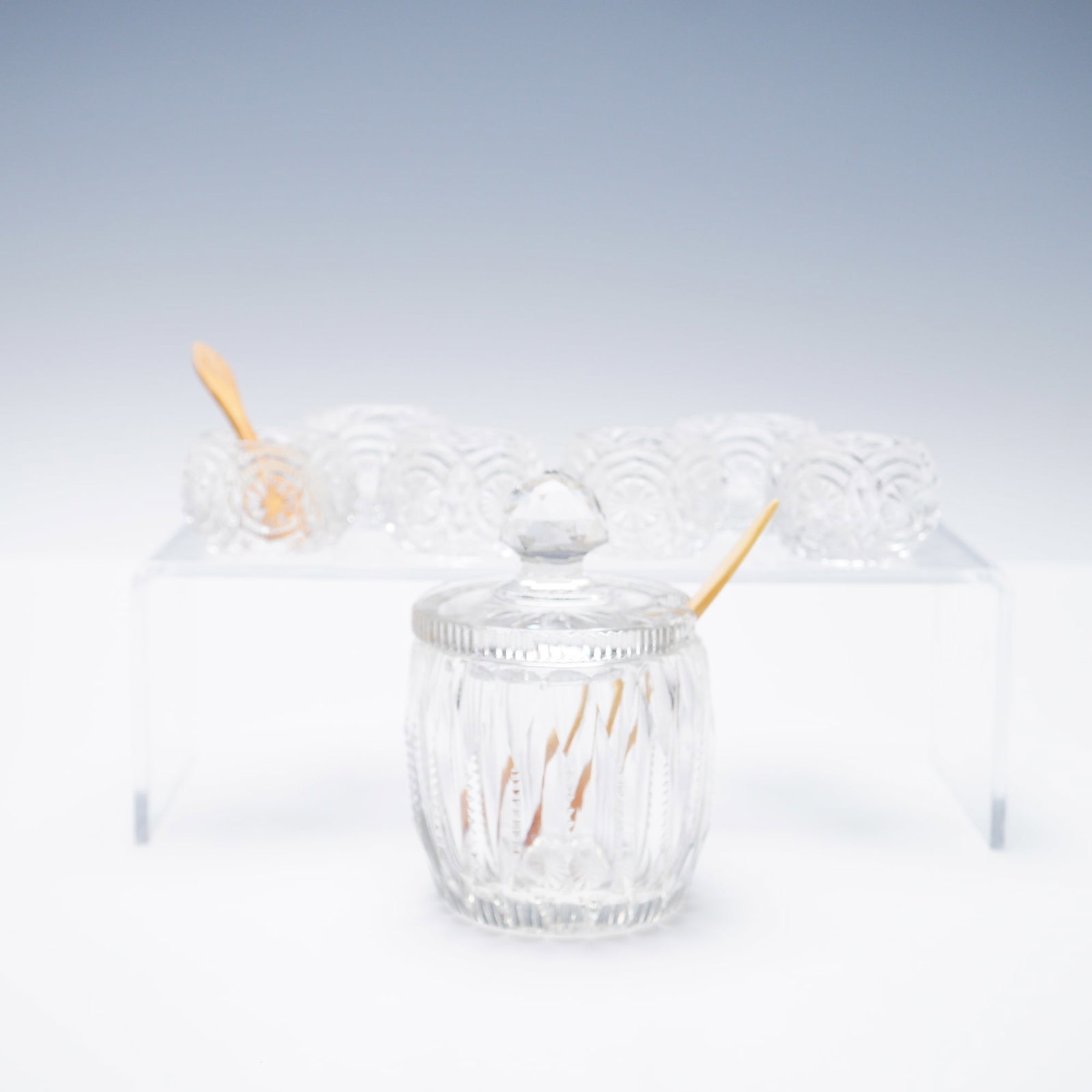 10pc Cut Glass Mustard Jar With Lid, Spoons, and Salt Cellars: A finely cut glass serveware set featuring a mustard jar with faceted lid and matching spoon, accompanied by six cut glass salt cellars that share a small serving spoon. Each piece showcases detailed