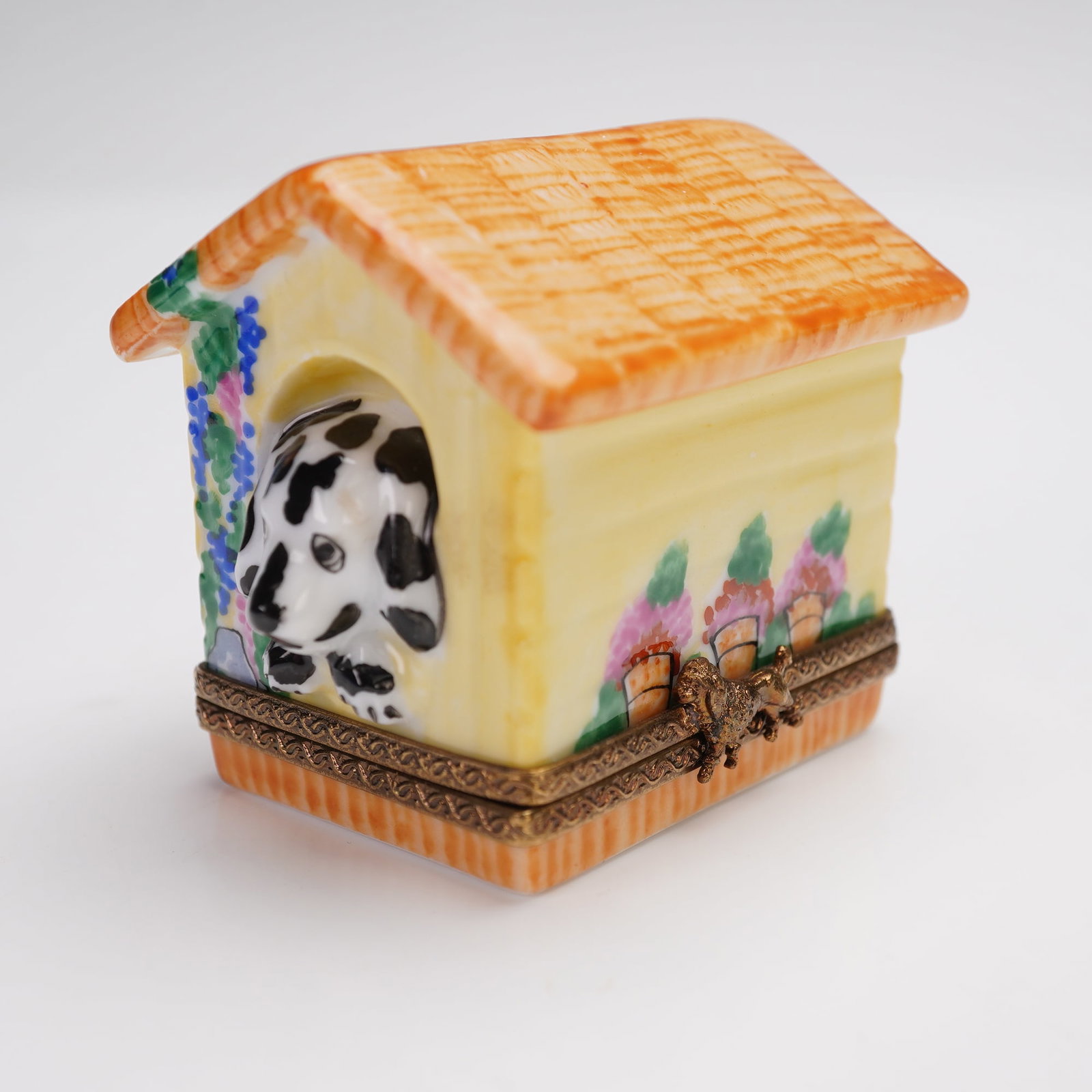 Limoges France Floral Doghouse Treasure Box: Porcelain trinket box in the form of a doghouse with a black and white dog peeking from the entrance. The exterior is decorated with floral and potted plant motifs on all sides, and the hinged lid fea