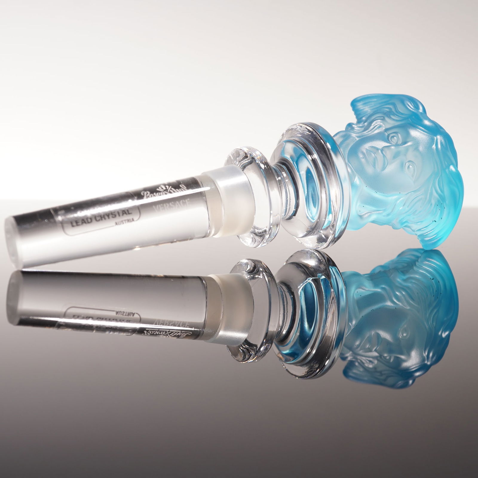 Rosenthal Versace Crystal Stopper, Blue Medusa: A luxury Rosenthal Versace crystal bottle stopper featuring the iconic Medusa head in frosted blue crystal. The stopper is crafted from over 24 percent lead crystal, made in Austria, and bears the Ver