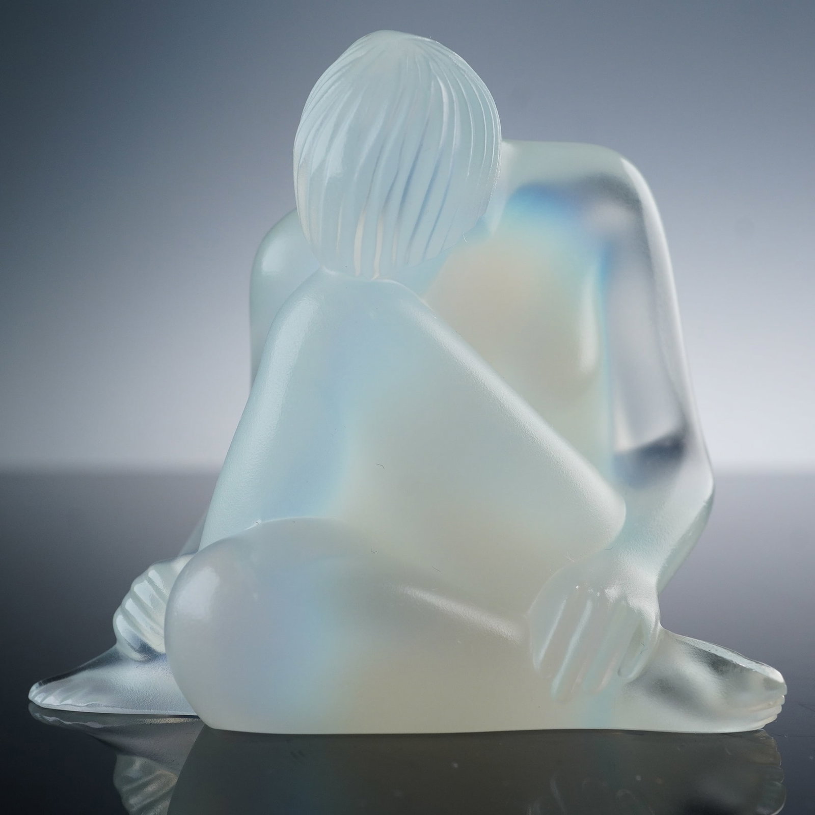 Lalique Opalescent Crystal Nude Figurine, Reve: This exquisite Lalique piece is titled Reve, presenting a seated nude rendered in frosted opalescent crystal with delicate highlights of color that shift in the light. The sculptural form emphasizes s