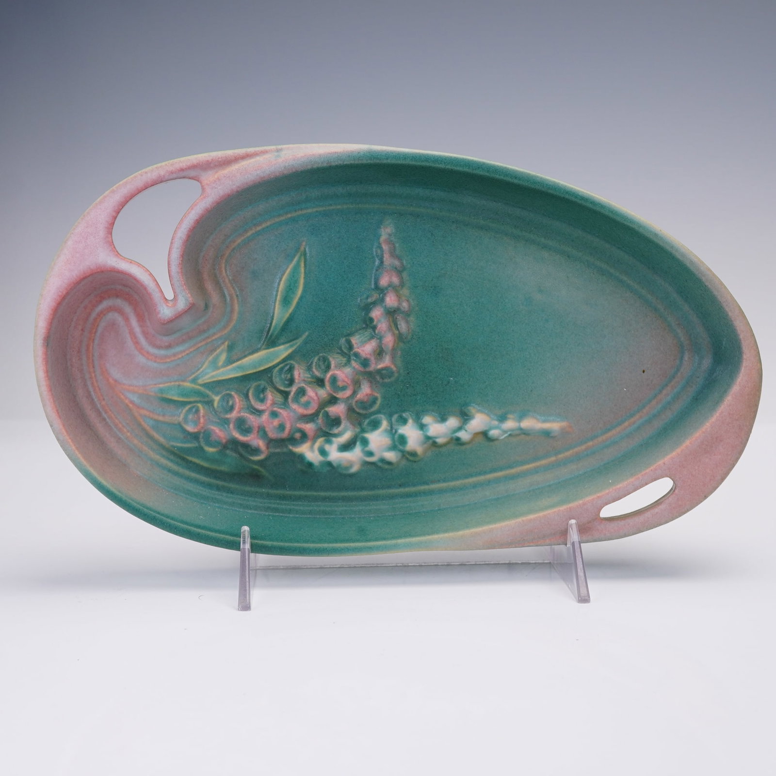 Roseville Pottery Foxglove Green and Pink Tray: This Roseville Pottery tray from the Foxglove line features a soft green and pink glaze highlighted by raised clusters of foxglove blossoms and foliage. The elongated form with integrated handles make