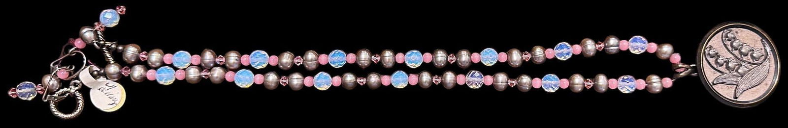 A beautiful handmade necklace with a button: 1 Long crystal glass example with a floral button. This beautiful pink and iridescent beaded necklace is adorned with a 19th century brass and pewter Lily of the valley button. Issued: DIVISION 1=PRE