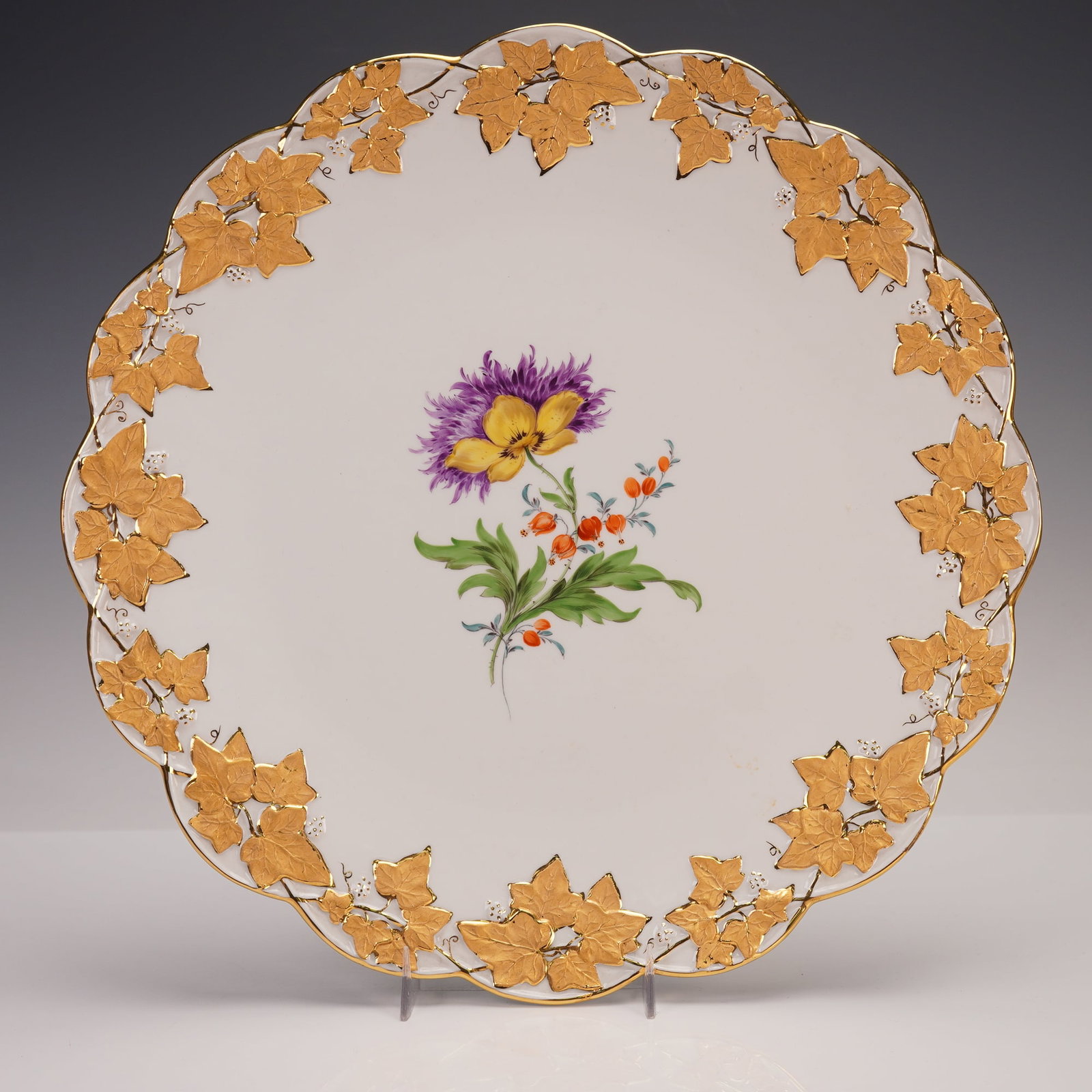 Meissen Porcelain Floral and Gilt Cabinet Plate: A finely decorated Meissen porcelain cabinet plate with scalloped rim, painted at the center with a colorful floral spray and bordered by raised gilt ivy leaves and trailing vines. The rich gold detai