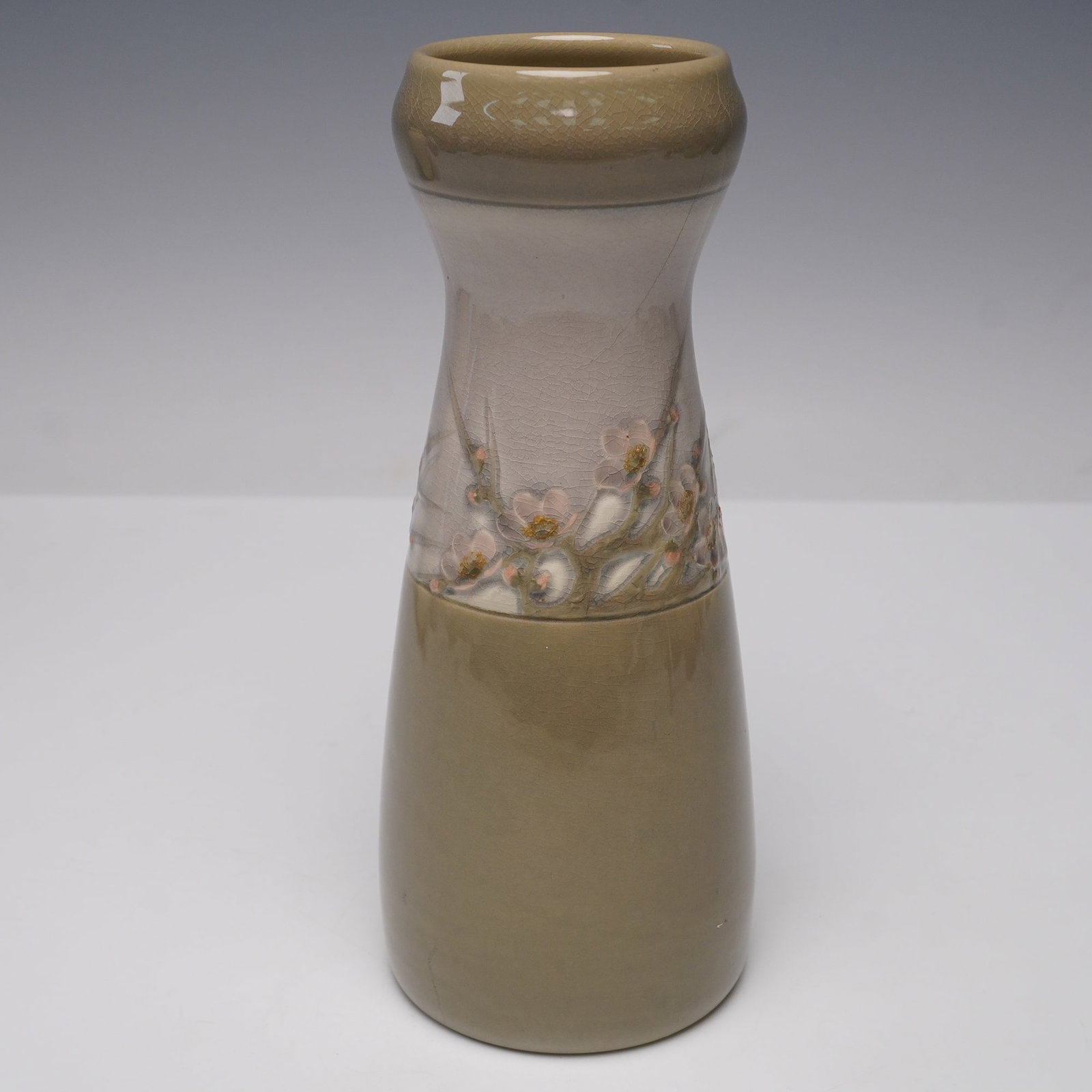 Rookwood Floral Crocus Vase, 1656E: A tapering ceramic vase with a wide rim, finished in a two-tone glaze of muted olive and gray. The upper section features delicate raised floral decoration depicting crocus blossoms in soft pink and w