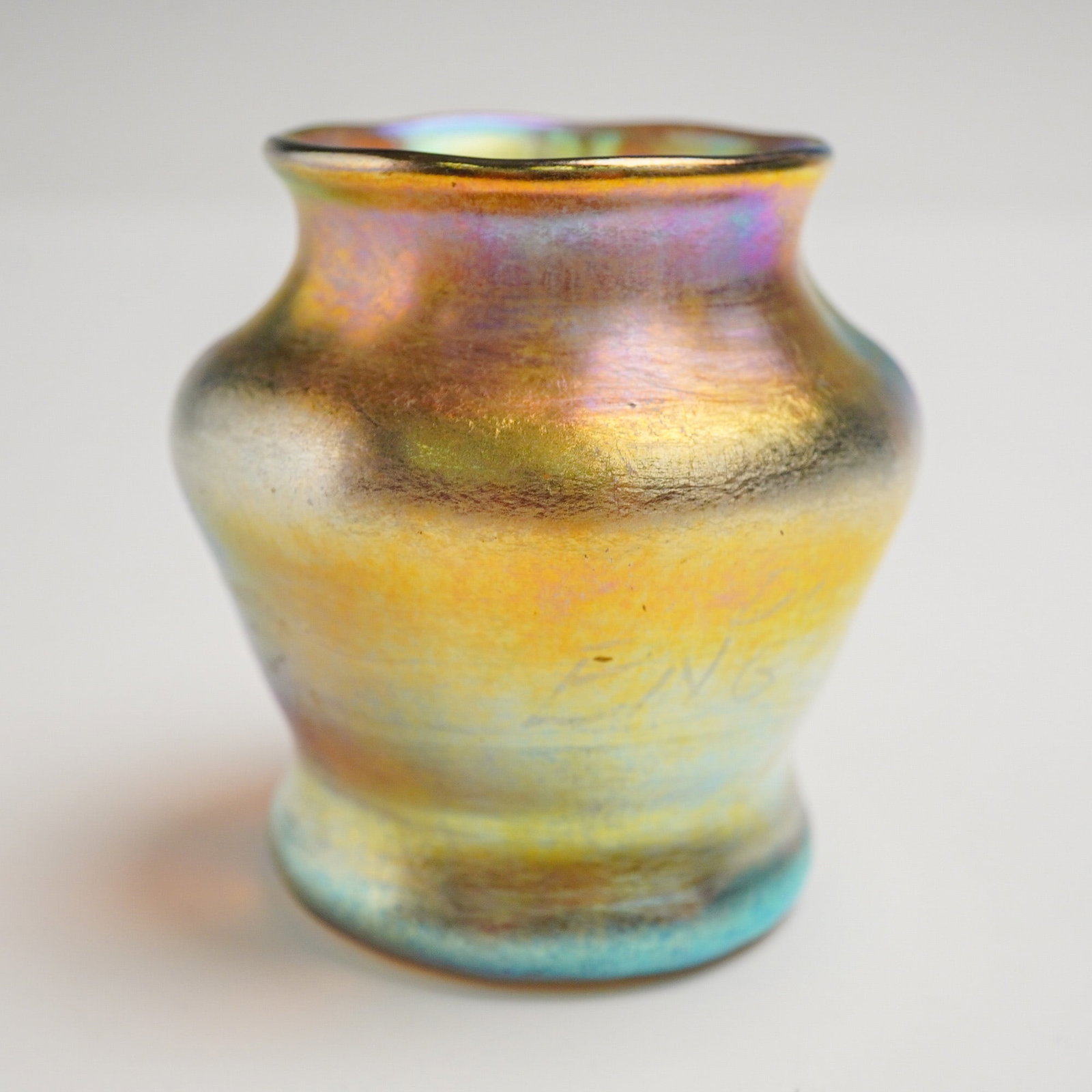 Louis Comfort Tiffany Favrile Glass Iridescent Small Vase: Exhibiting a rounded body with a slightly tapered base and flaring rim, executed in lustrous gold and amber tones with surface hues shifting to violet, blue, and green under light. The glass displays 