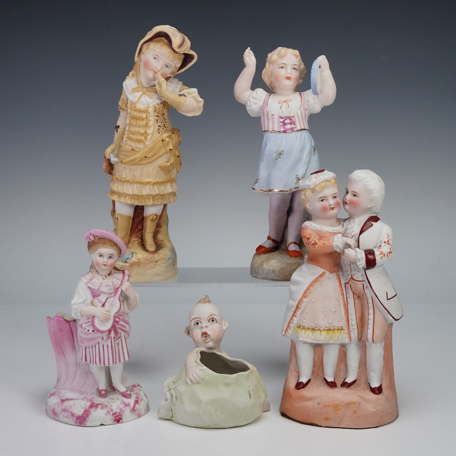 5pc Ceramic European Art Figurines and Toothpick Holders: A set of three porcelain figurines and two toothpick holders. The figurines include a girl in a golden ruffled dress, a child in a striped bodice with blue skirt, and a couple dancing in coordinated a