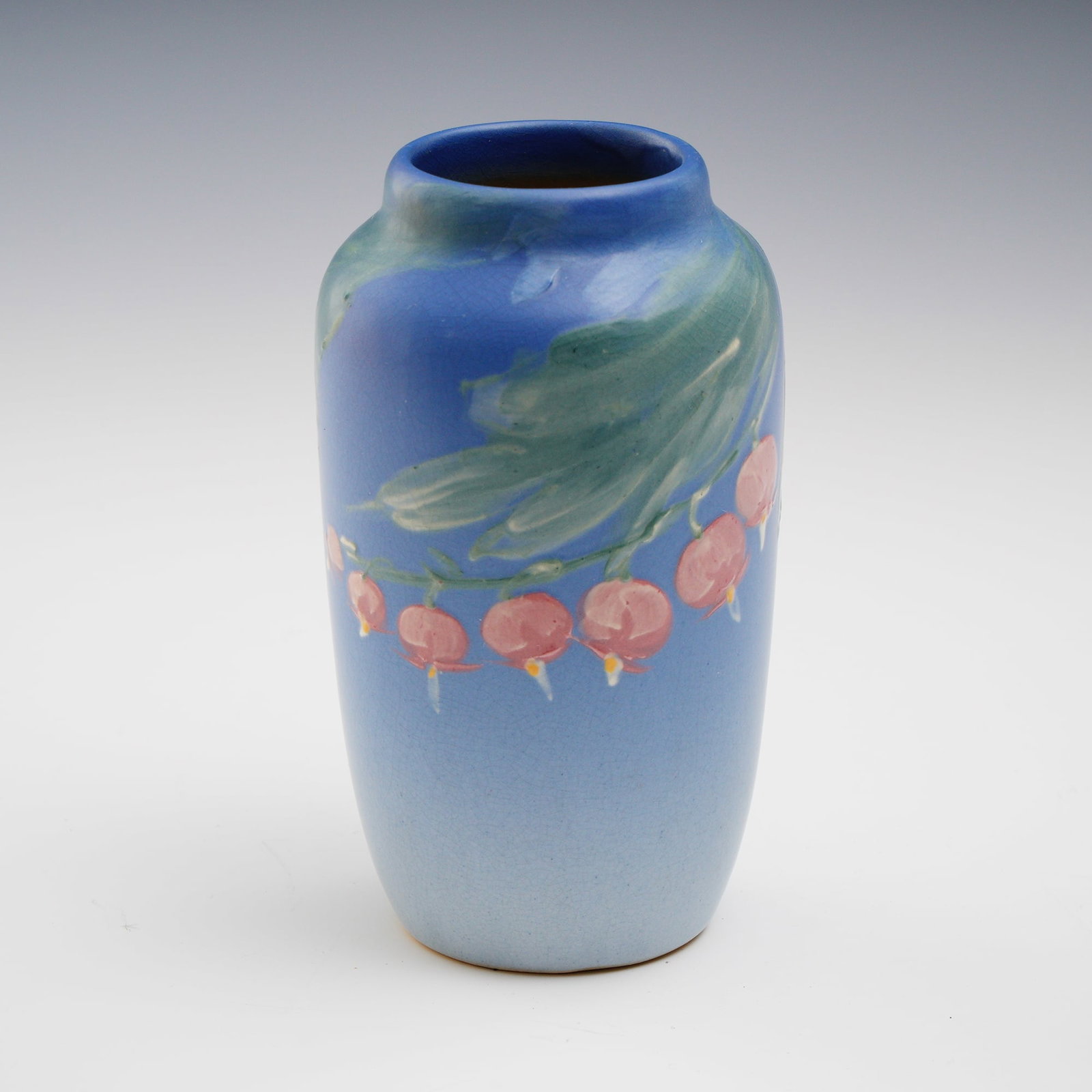 Weller Pottery Vase with Hand Painted Floral Design: A charming example of Weller Pottery, this hand painted vase features a rich blue ground with trailing pink blossoms and green foliage, executed in the soft, painterly style for which Weller is celebr
