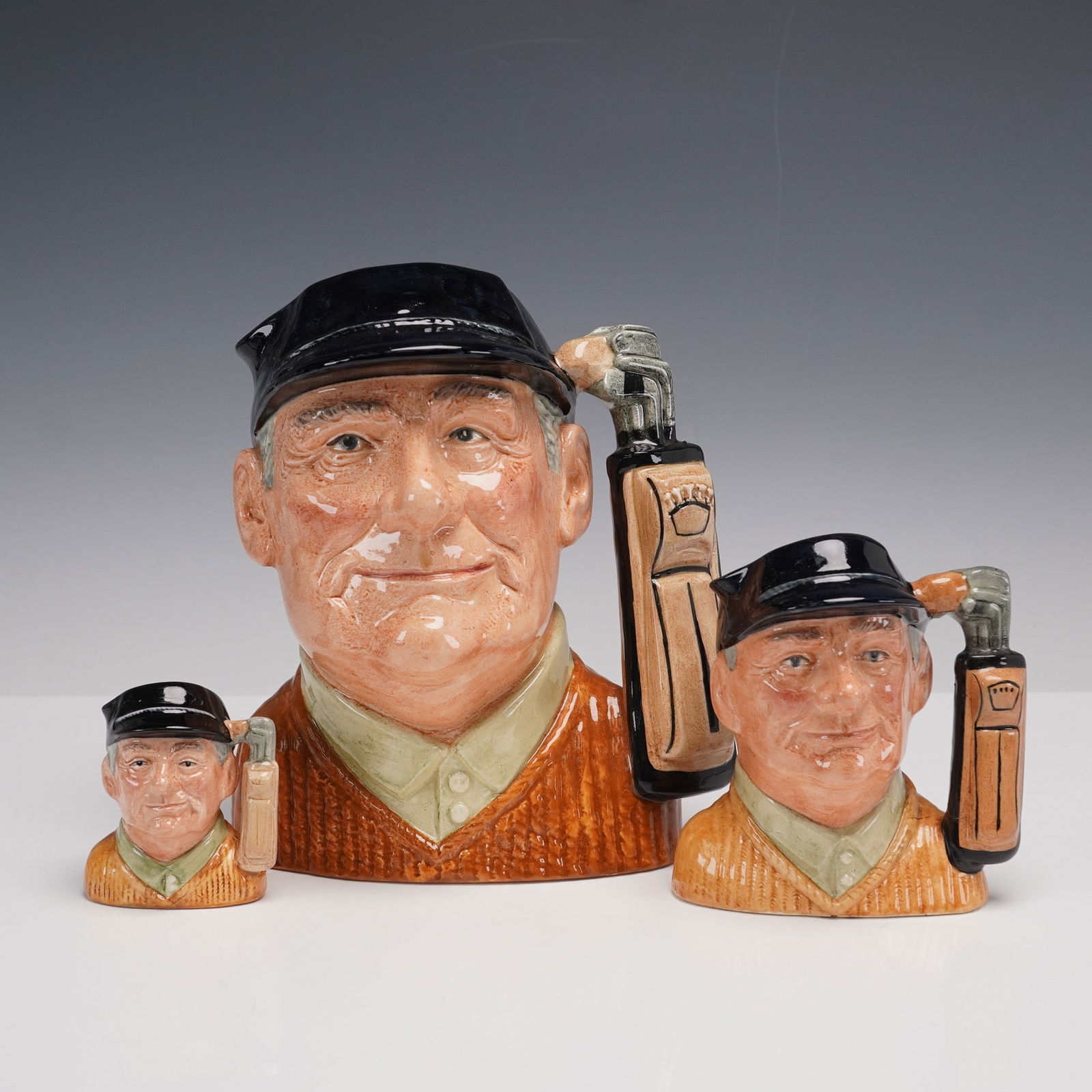 3pc Royal Doulton Character Jugs, Golfer D6623, D6756 & D6757: Set of three Royal Doulton character jugs depicting The Golfer, designed by David B. Biggs. The grouping includes the large (D6623), small (D6756), and miniature (D6757) sizes. Each jug portrays a smi