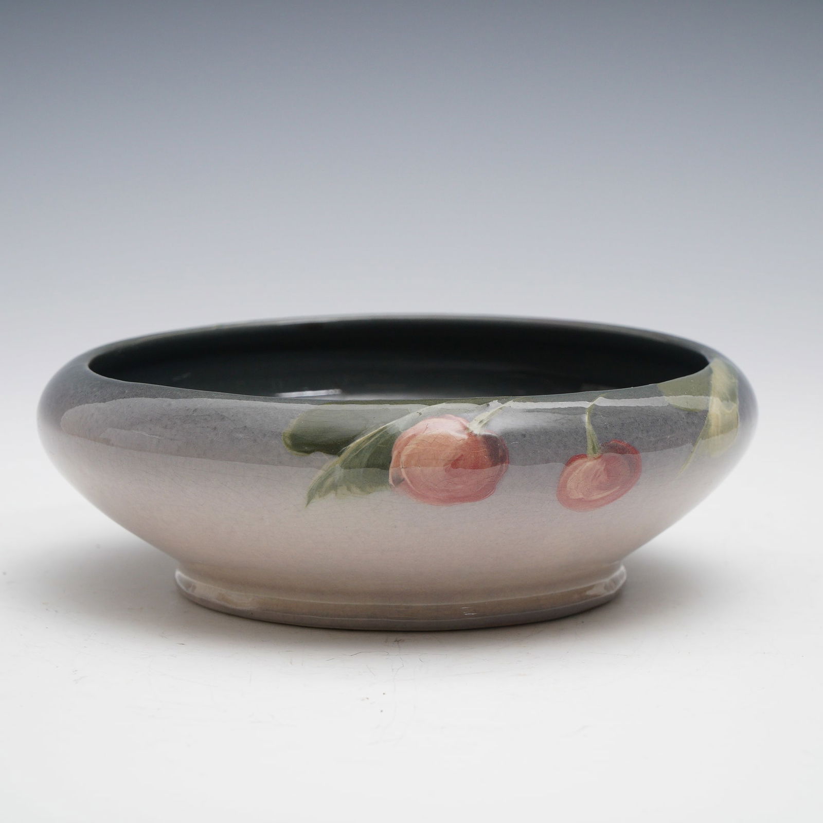 Weller Pottery Louwelsa Cherry Bowl: Weller Pottery Louwelsa bowl, decorated with hand-painted cherries and leaves against a softly blended background glaze. The interior is finished in a deep glossy brown to black, while the exterior fe
