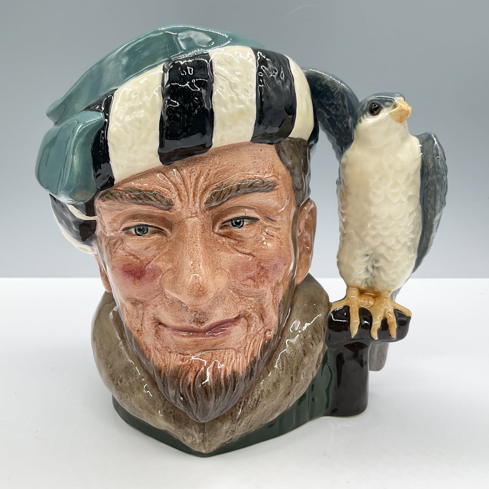 Falconer D6533 - Large - Royal Doulton Character Jug: Variation One. Green with black and white striped fur hat, green coat, grey and white falcon. Royal Doulton backstamp. Artist: Max Henk Issued: 1960 - 1991 Dimensions: 7.5"H Country of Origin: England