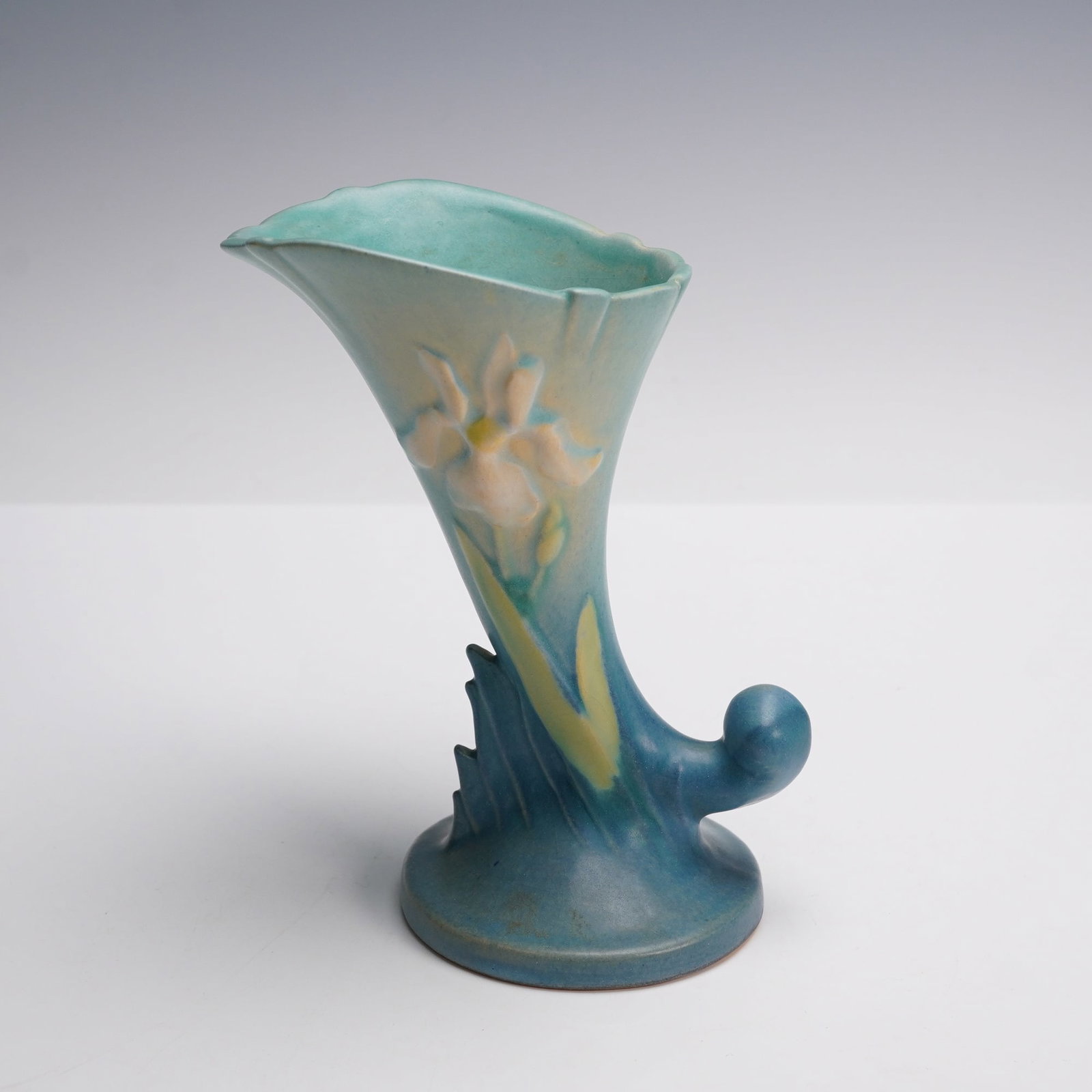Roseville Pottery Blue Zephyr Lily Cornucopia Vase, 131-6: This art pottery piece features a flaring cornucopia form with a stylized scrolled base, decorated in soft matte blue and green glazes. The front and back display raised lily blossoms in pastel tones 