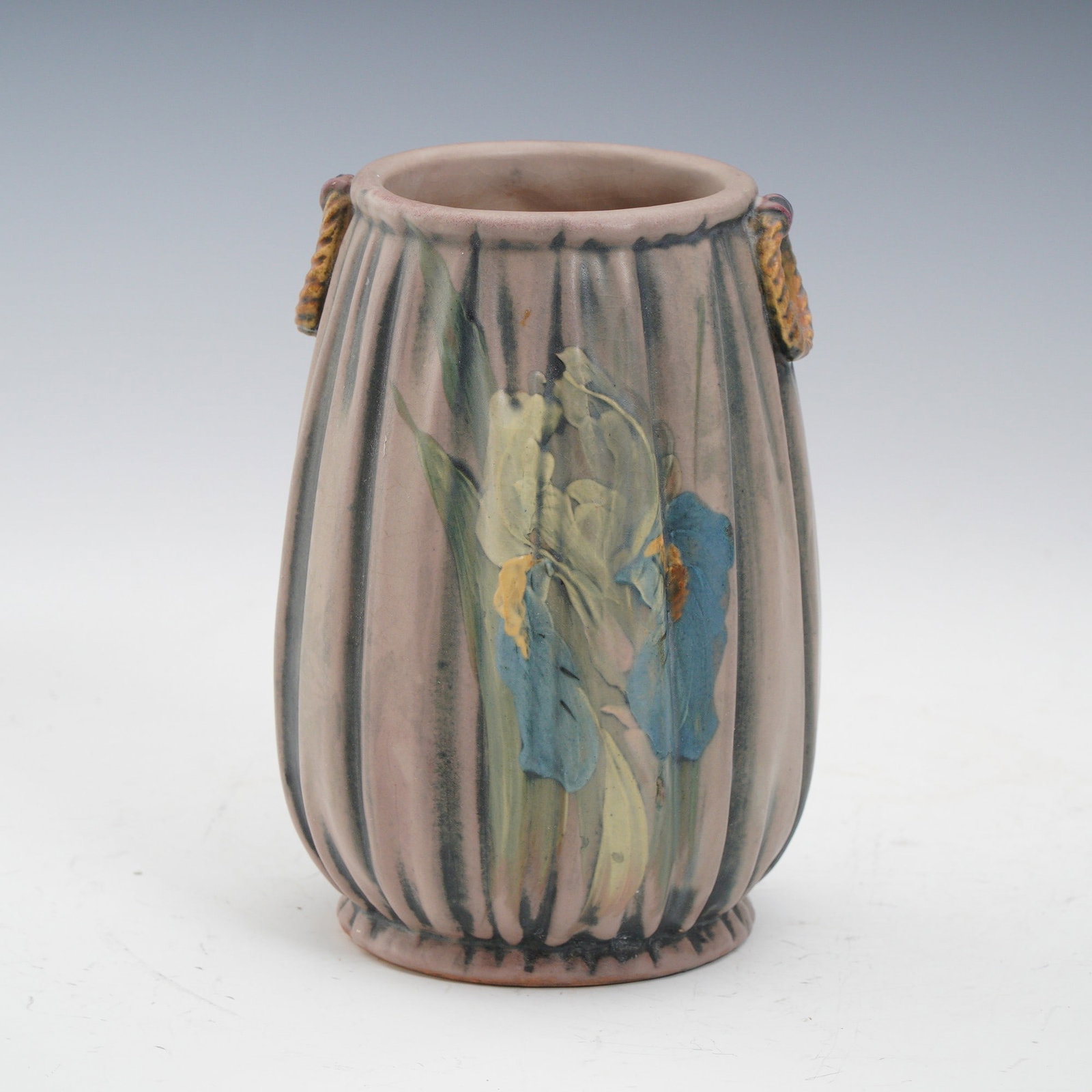 Weller Pottery Louella Ribbed Vase: A Weller Pottery Louella vase featuring a softly ribbed body with applied rope-twist handles at the shoulder. The piece is decorated with a hand-painted iris motif in muted shades of blue, yellow, and