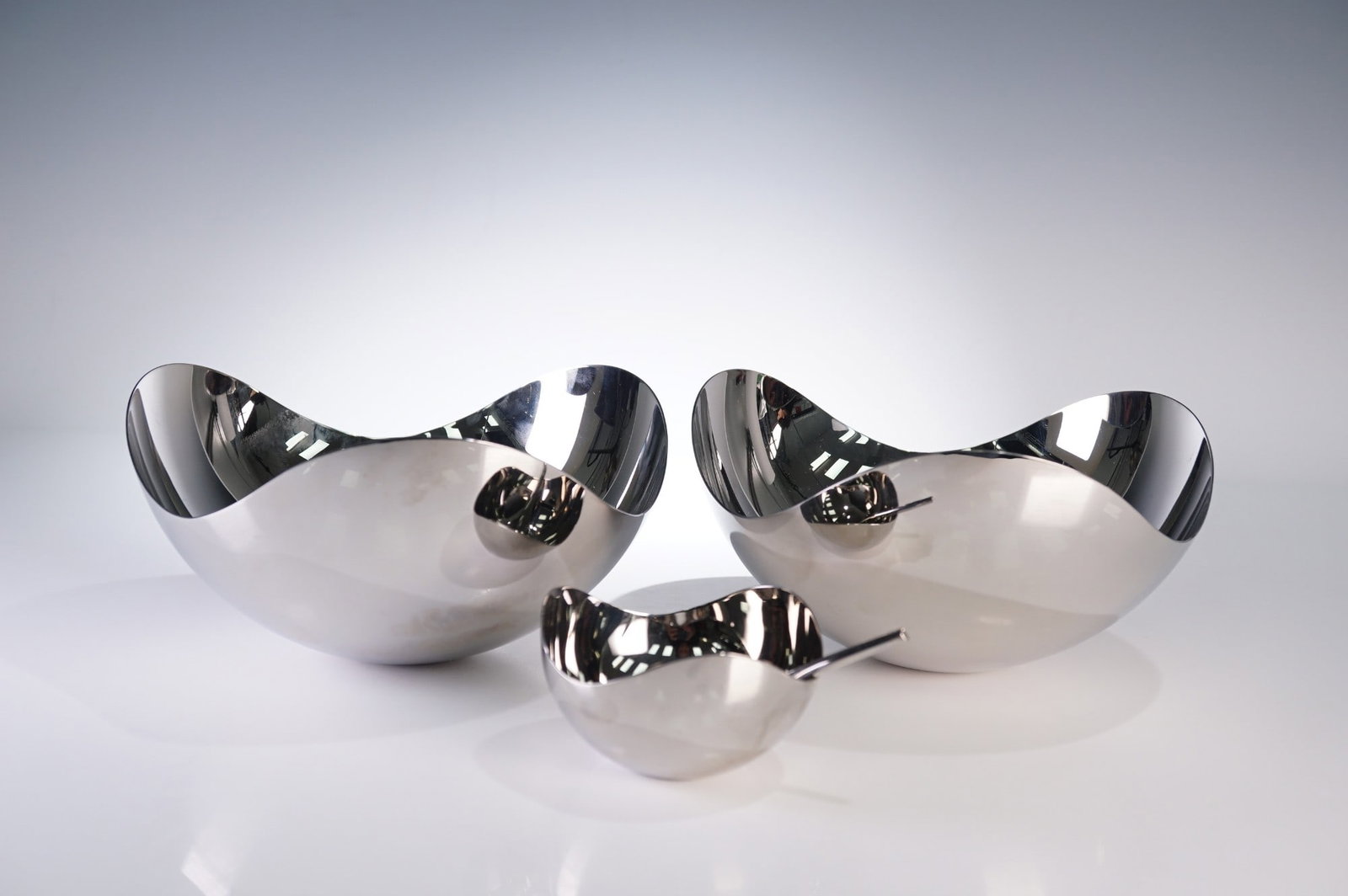 4pc Georg Jensen Bloom Collection Bowl and Spoon Set: A striking 4 piece Georg Jensen Bloom Collection set, crafted in mirror polished stainless steel with graceful organic curves inspired by nature. This modernist ensemble includes three sculptural bowl