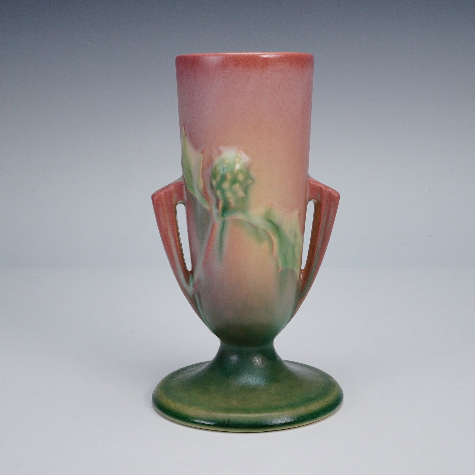 Roseville Pottery Pink Vase, Thornapple: Roseville Pottery Thornapple vase in a pink and green glaze with relief decoration of thornapple leaves and buds, the tapered form featuring double open handles rising to a flared rim, Roseville backs